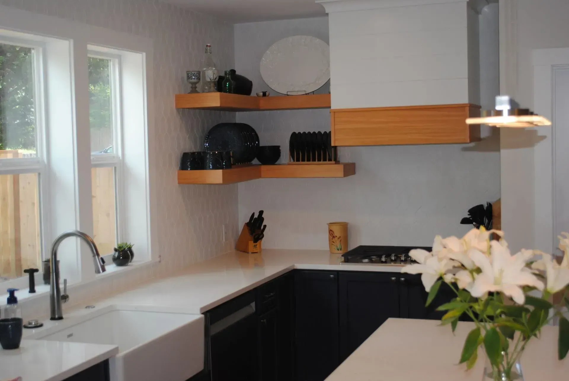 Bright modern kitchen with white cabinets, black shelves, and flowers on the counter