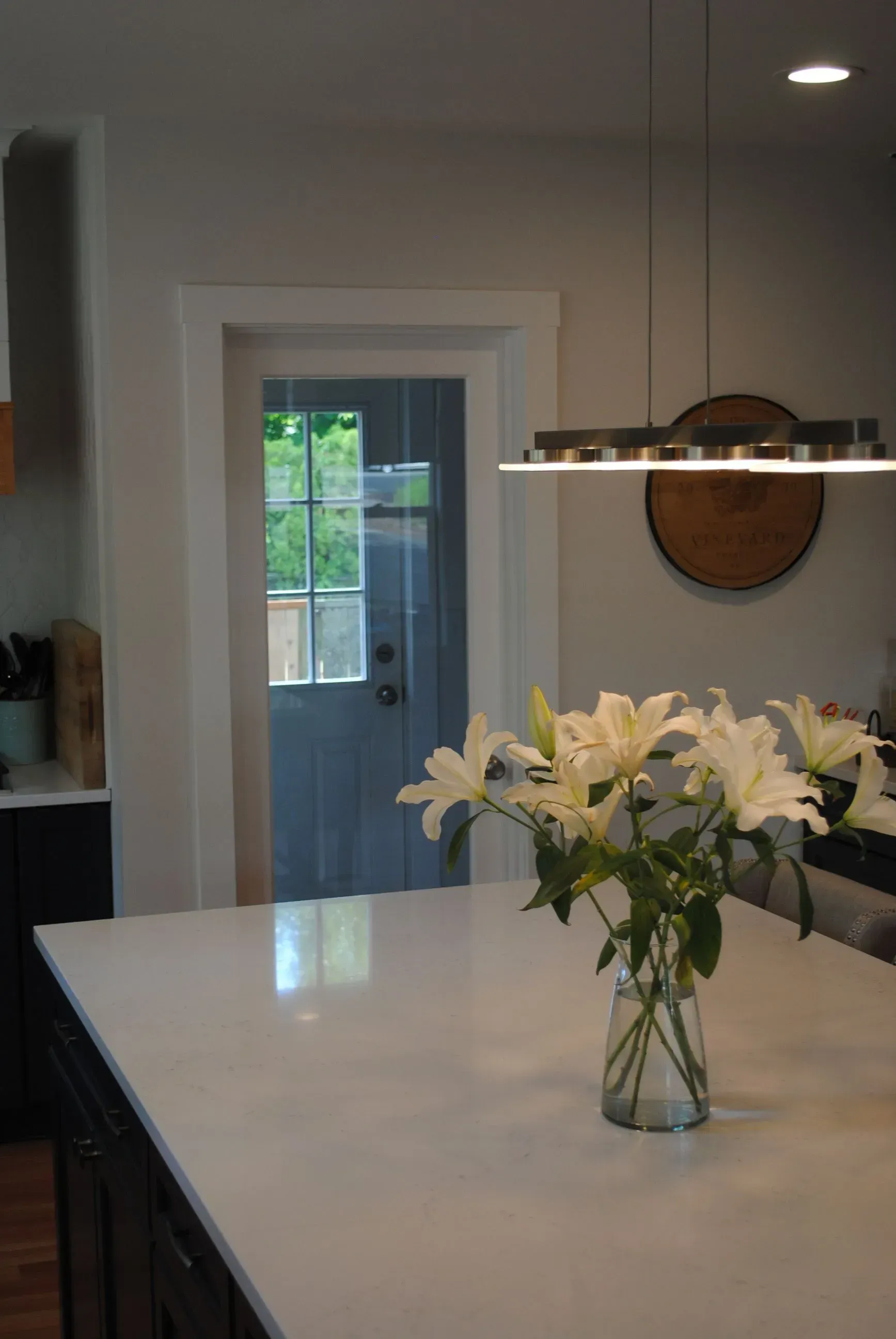 Modern kitchen with white island, vase of white flowers, and pendant light over the counter.