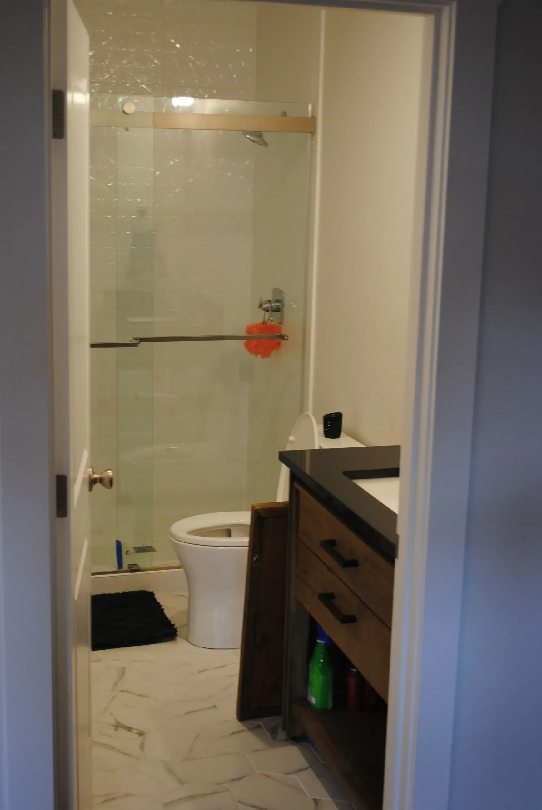 Small bathroom with a toilet, glass shower, and dark wood vanity beside the doorway.