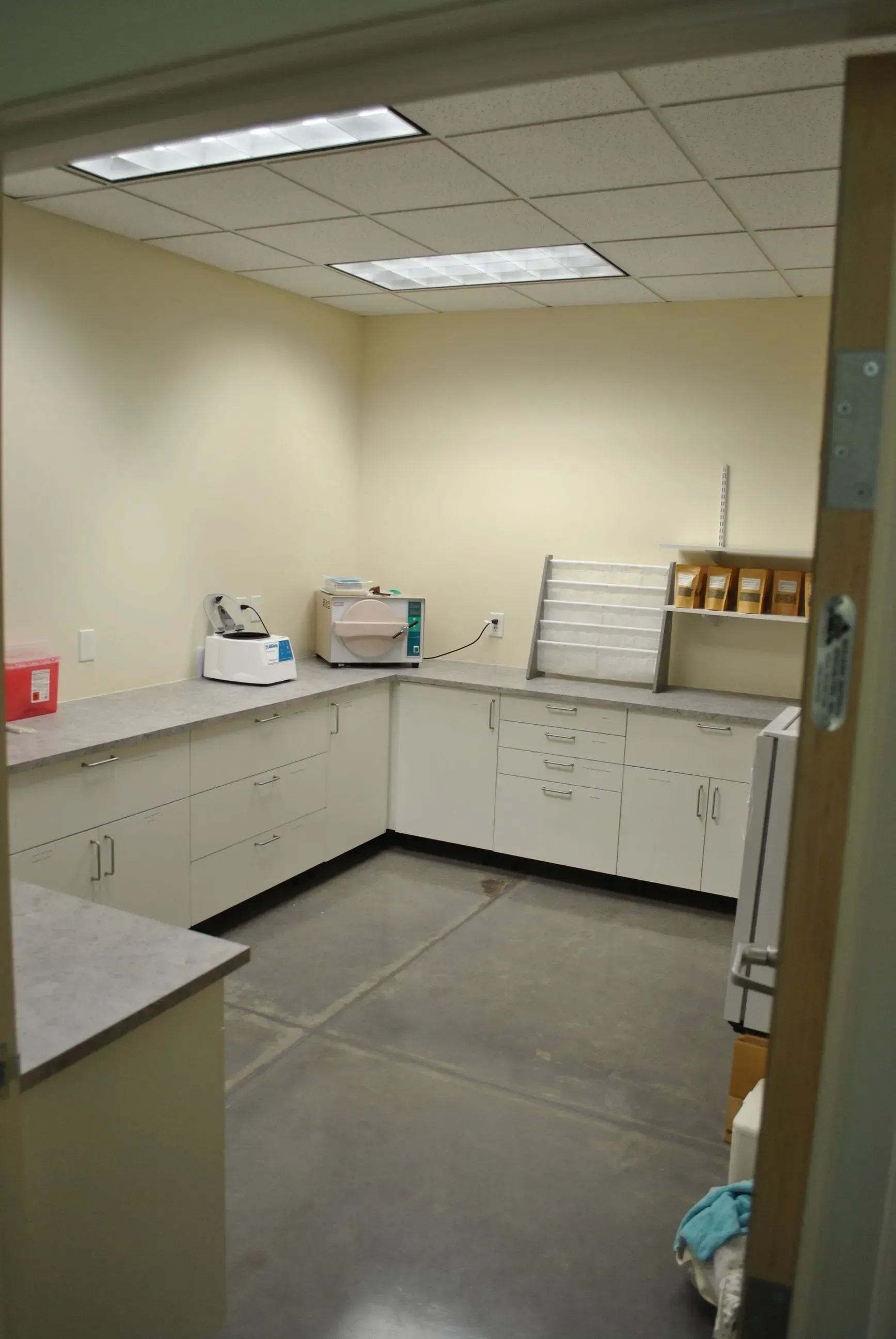 Empty office kitchenette with beige cabinets, countertop appliances, and fluorescent lighting