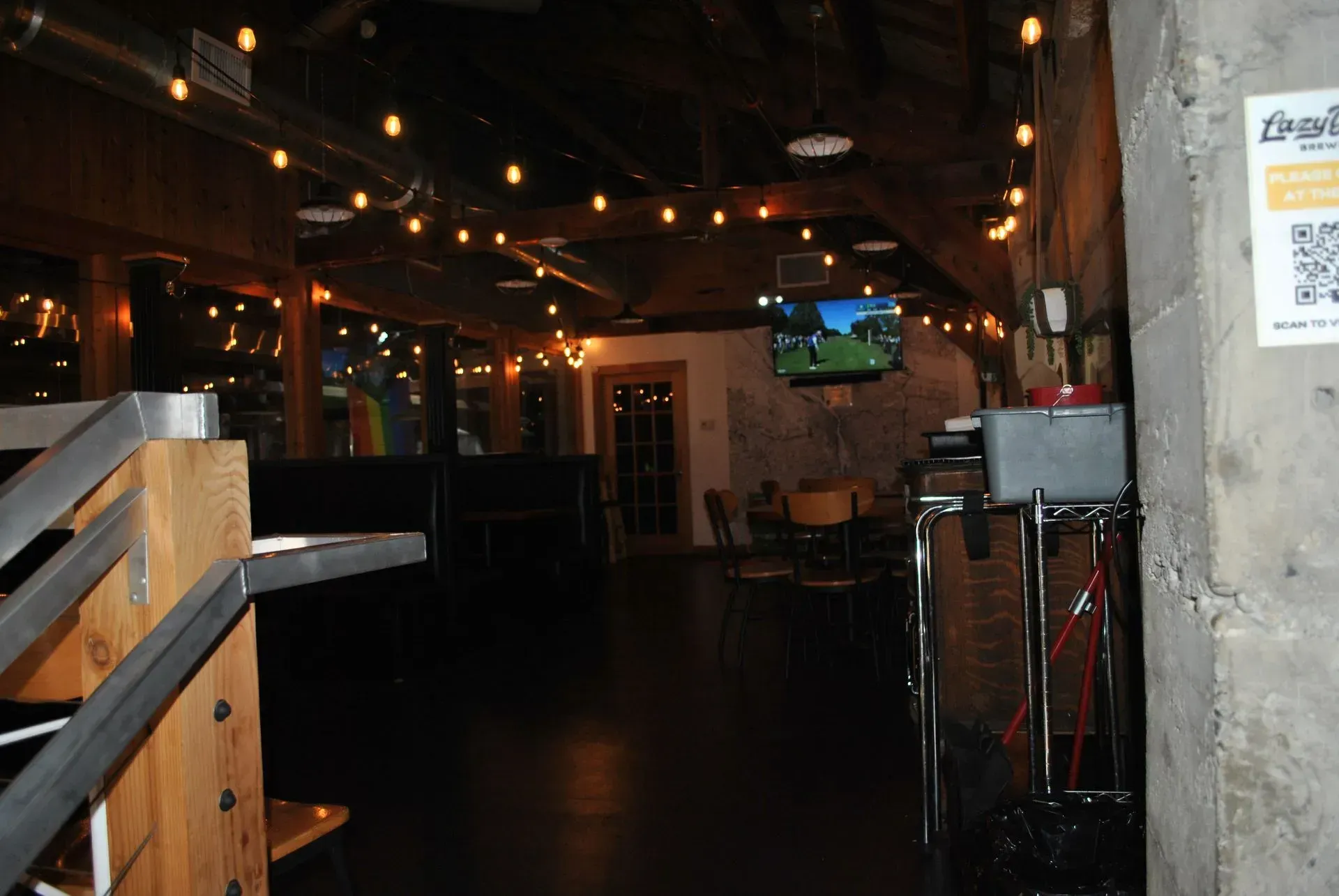 Dimly lit bar interior with string lights, wooden railing, and stools near a concrete wall