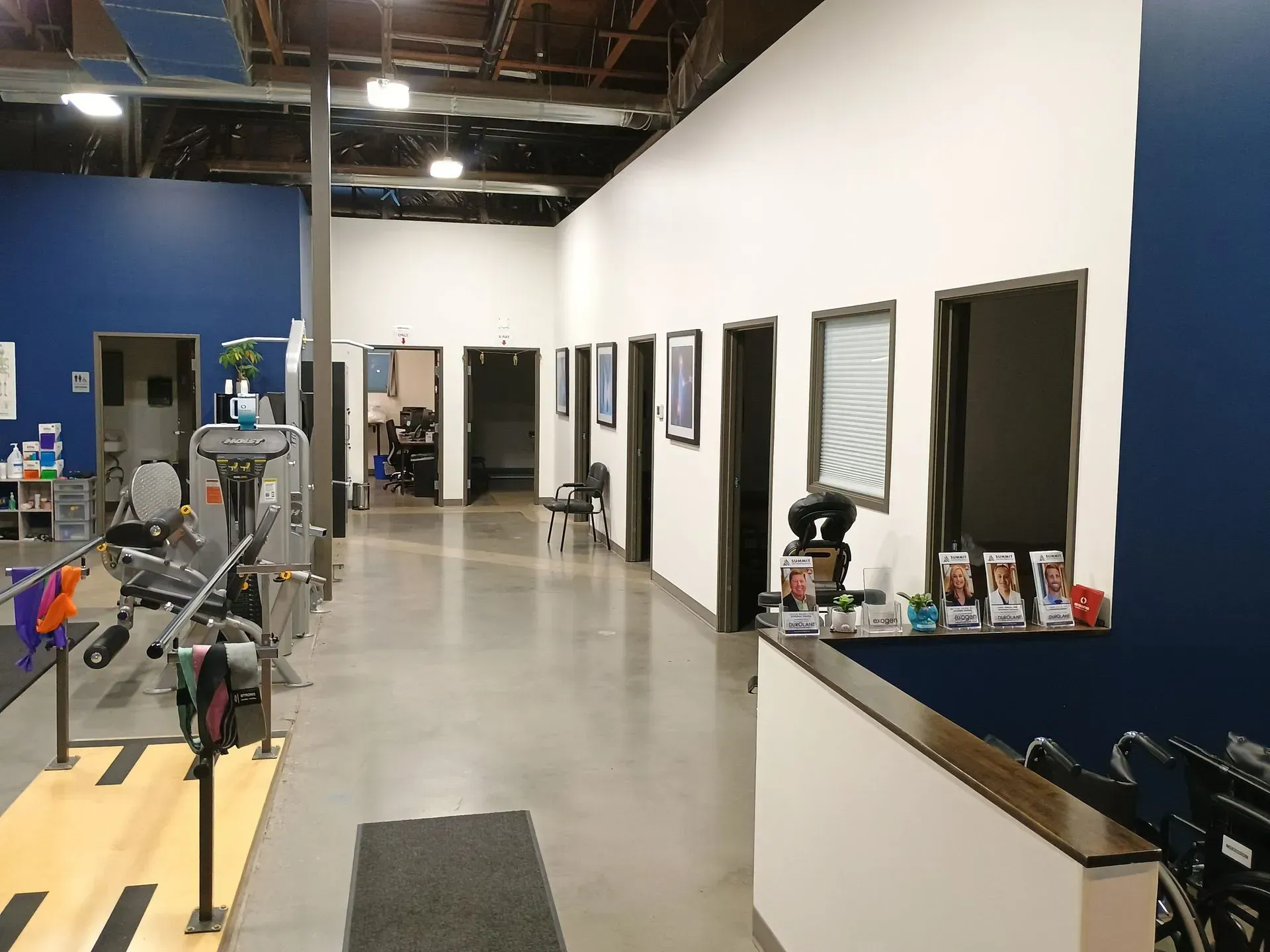 Warehouse-like office hallway with open doors, concrete floor, and equipment along the left side