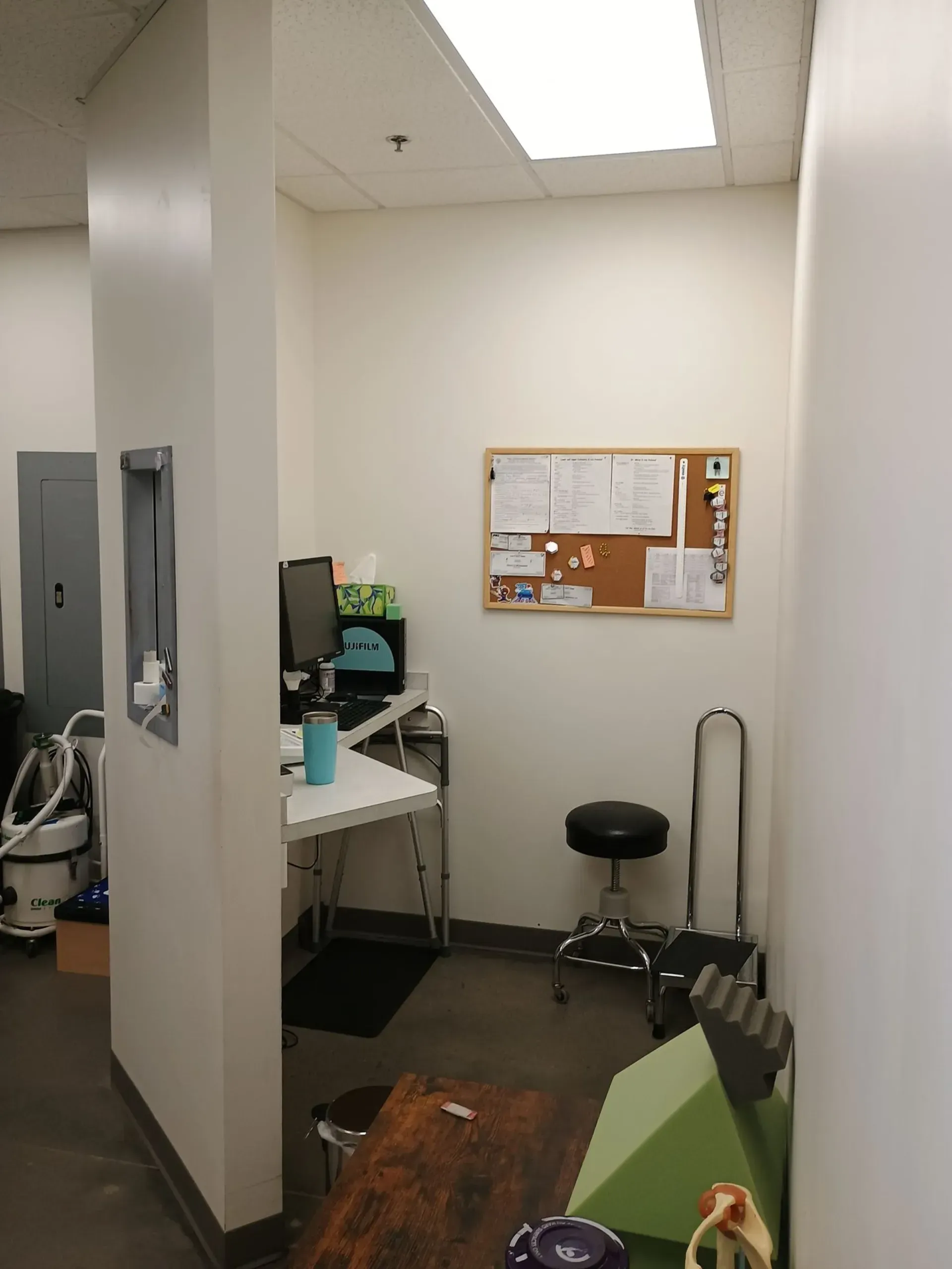 Small office corner with desk, stool, bulletin board, and green couch under fluorescent lights