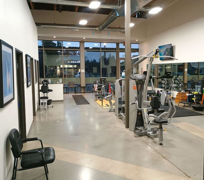 Modern gym interior with exercise machines, mirrored wall, and large front windows