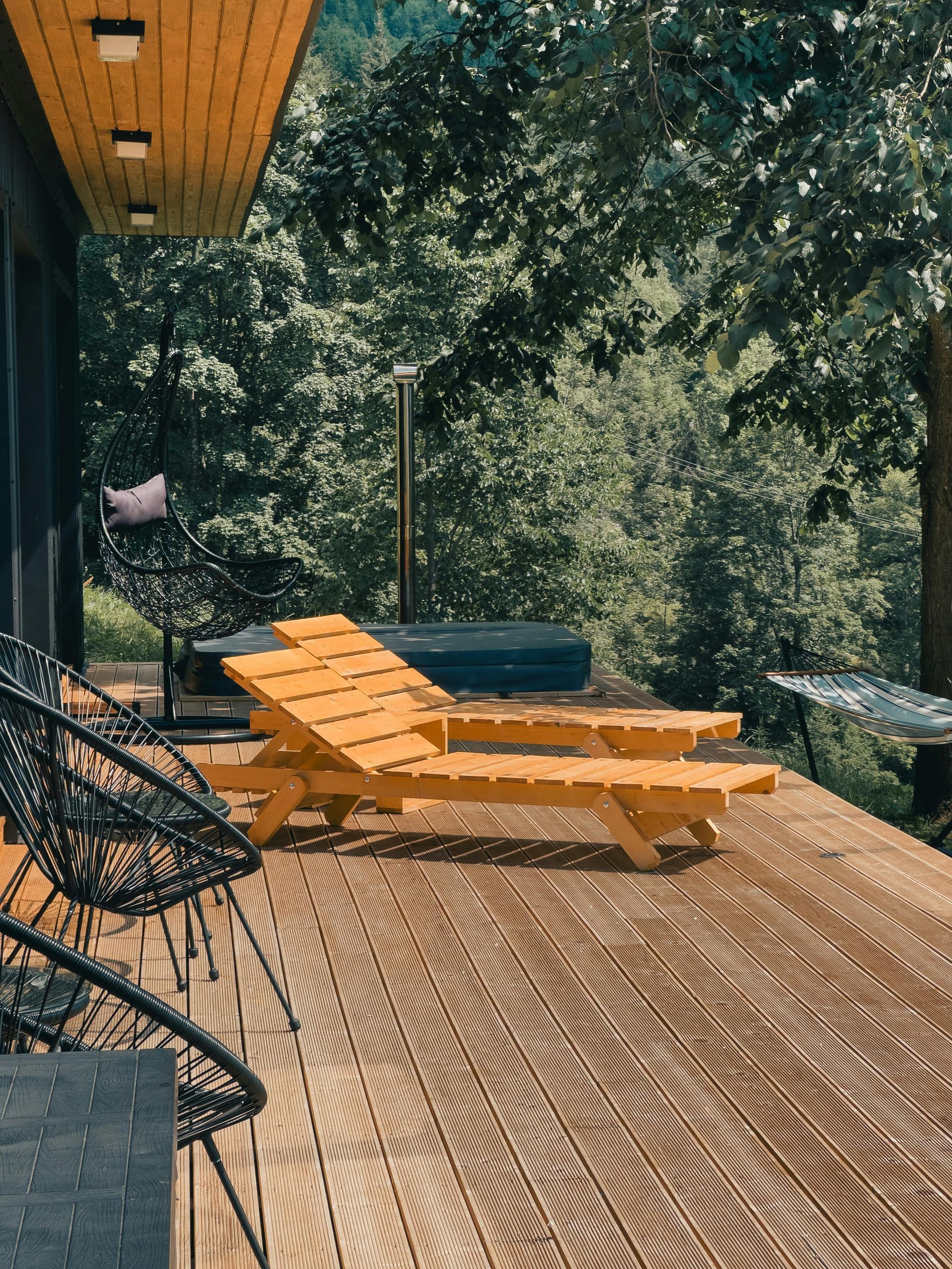 Wooden deck with lounge chairs under trees, overlooking a leafy outdoor setting.