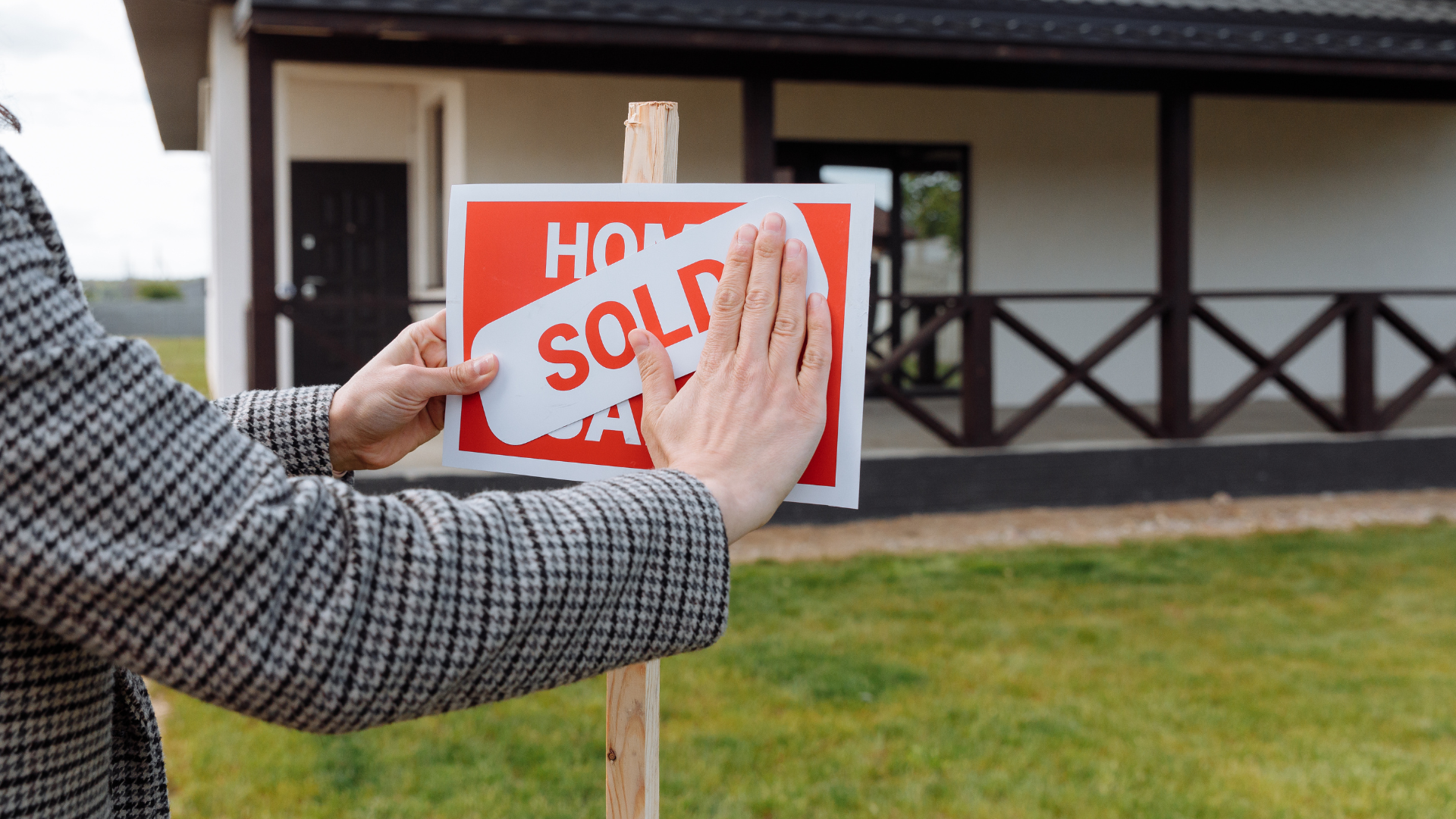 Hand holding house keys in front of a modern home for sale