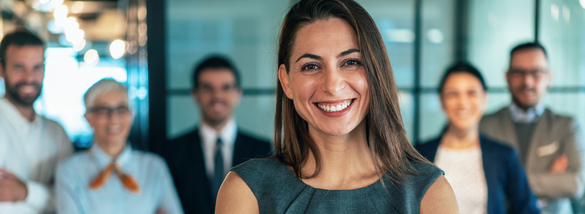 Mulher sorridente em frente a um grupo diversificado de pessoas em um escritório.
