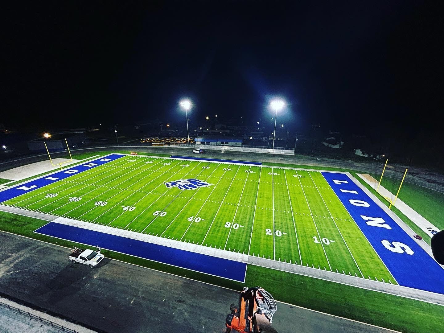 Nighttime football stadium with bright lights, green field, and blue end zones viewed from above