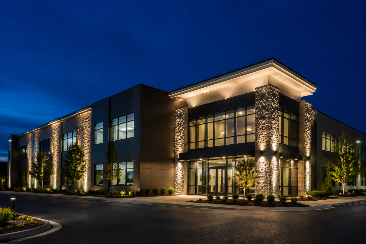 Modern office building at dusk with illuminated windows and stone facade under a dark blue sky
