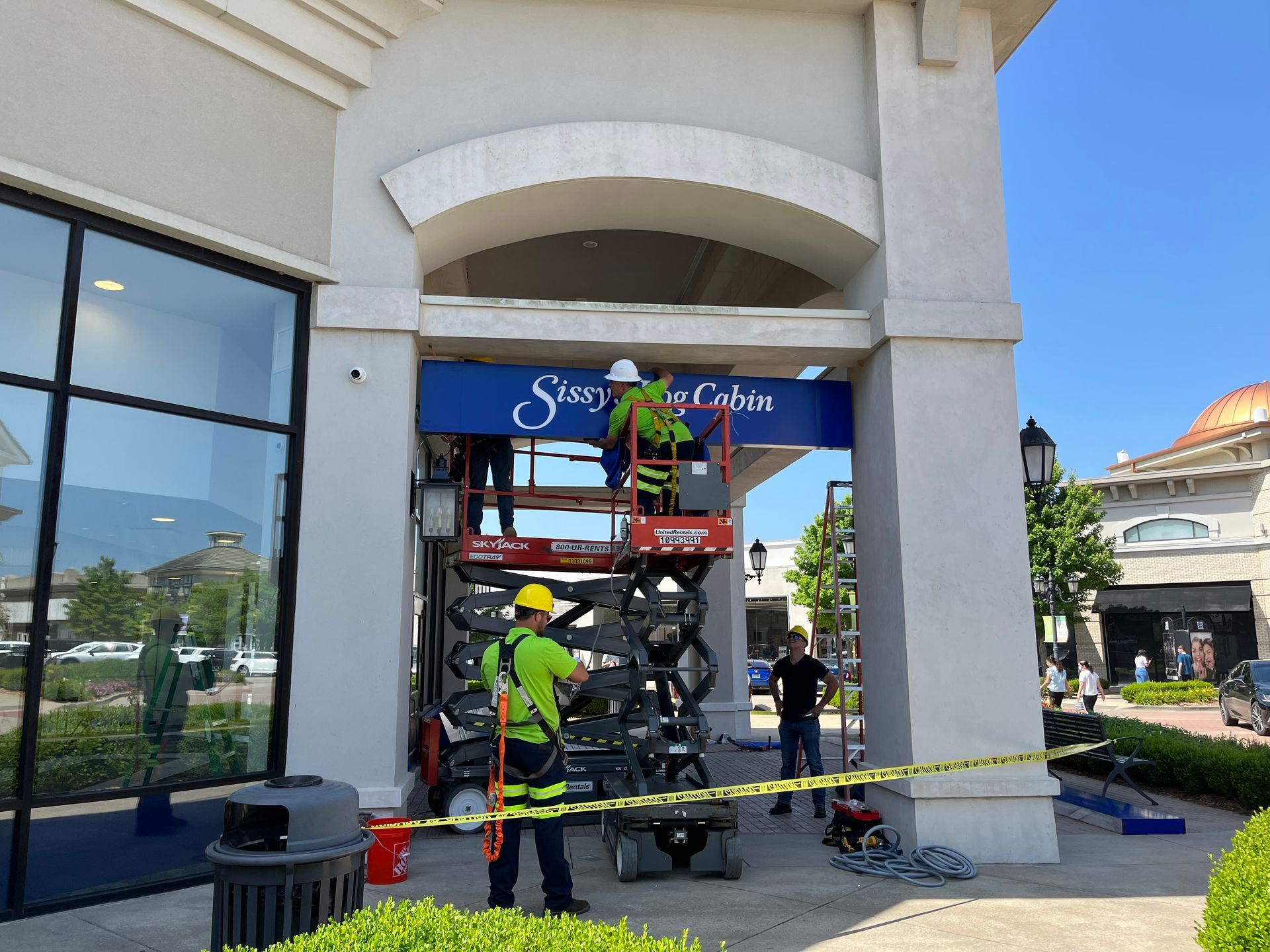 Firefighters in yellow gear work with a ladder at a building entrance beneath a café sign.