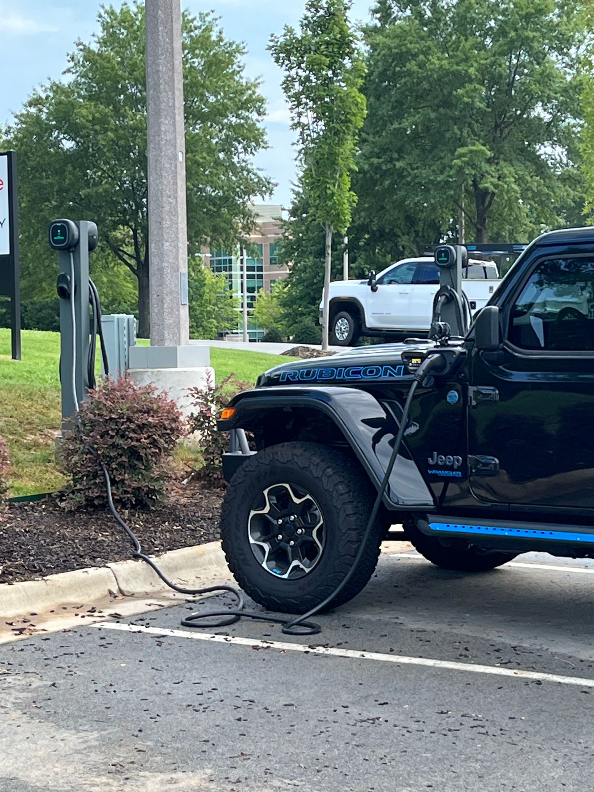 Black Jeep Wrangler parked by a sidewalk near a parking lot sign and greenery