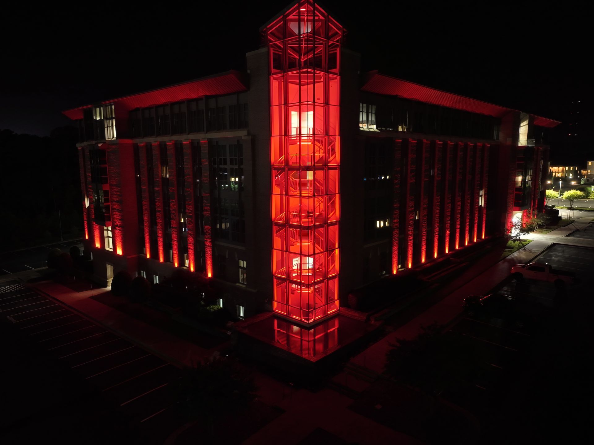 Night view of a building lit in red, with a glowing central glass tower.