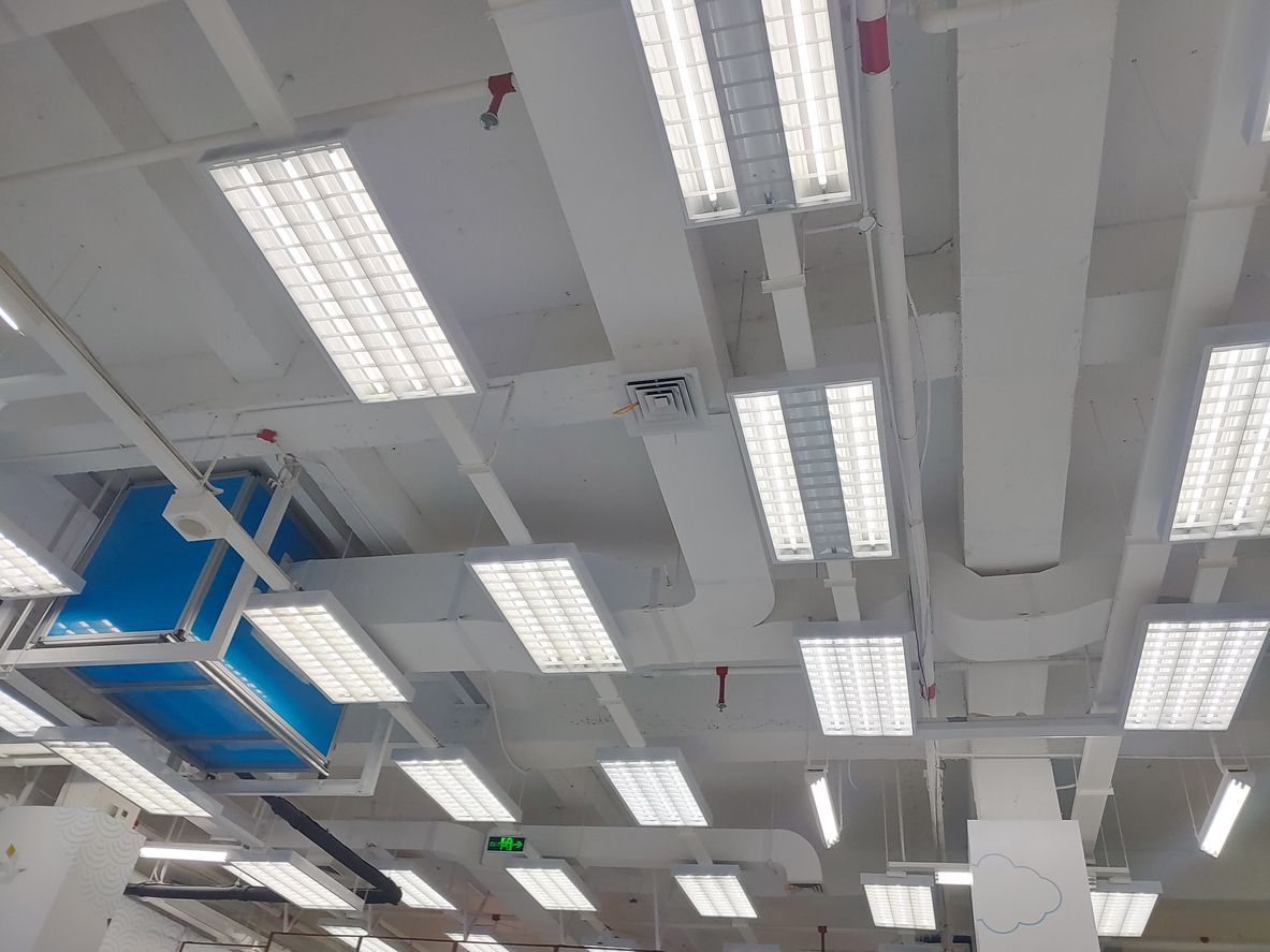Ceiling with bright fluorescent lights and blue ventilation ducts in an industrial indoor space