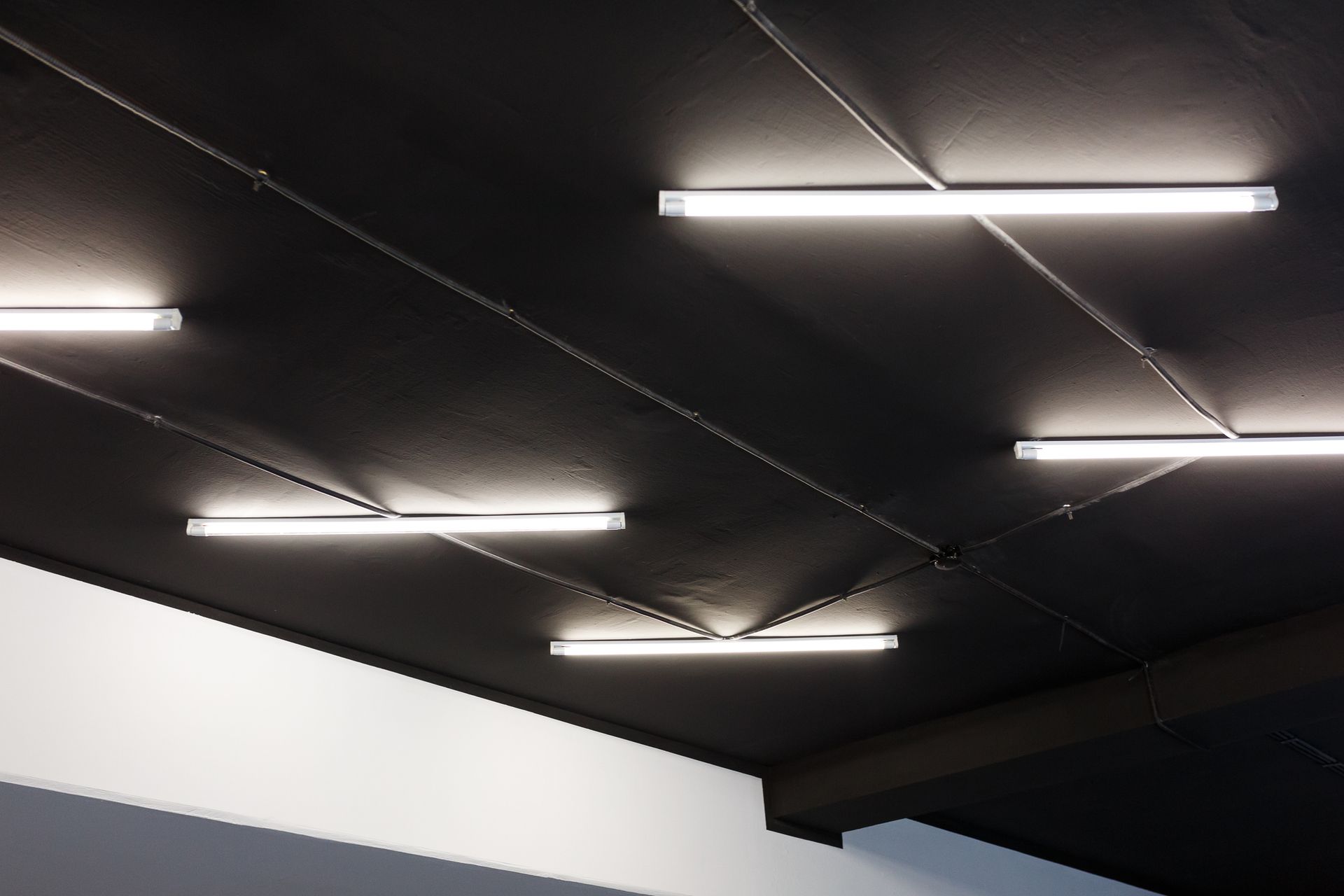 Black ceiling with several bright fluorescent strip lights in a modern indoor space