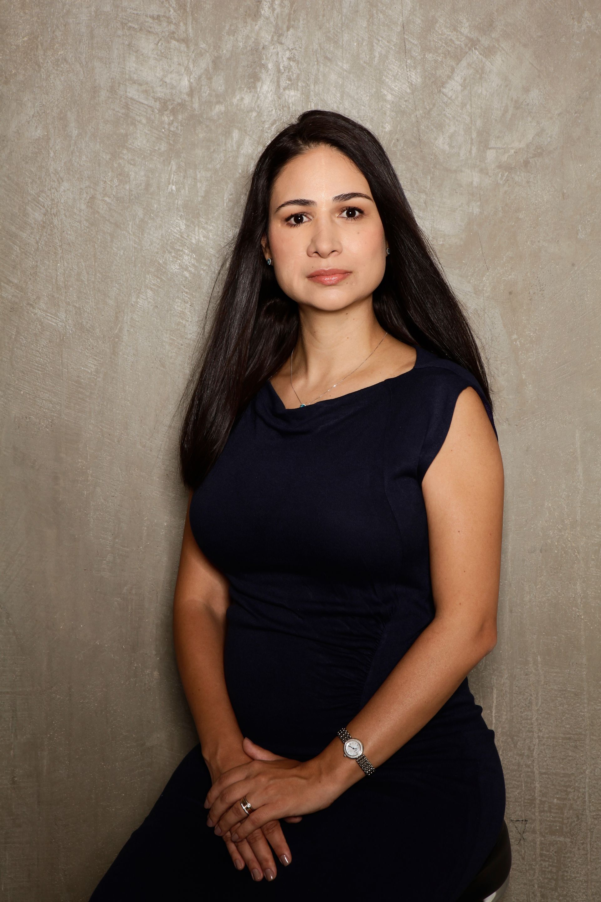 A woman in a blue dress is sitting on a stool with her hands on her knees.