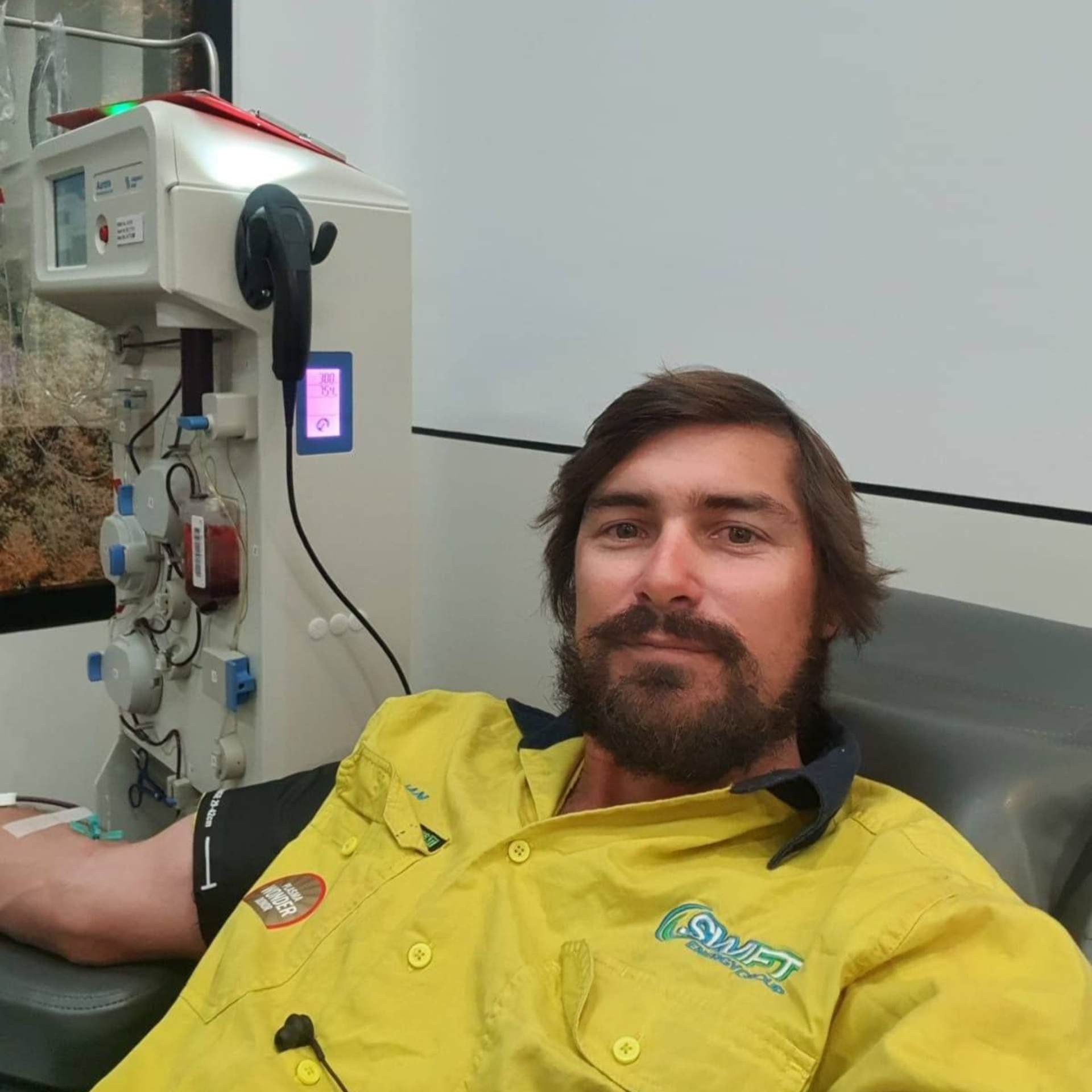 Man reclining in a chair giving blood, wearing a bright yellow Swift Energy Group shirt.