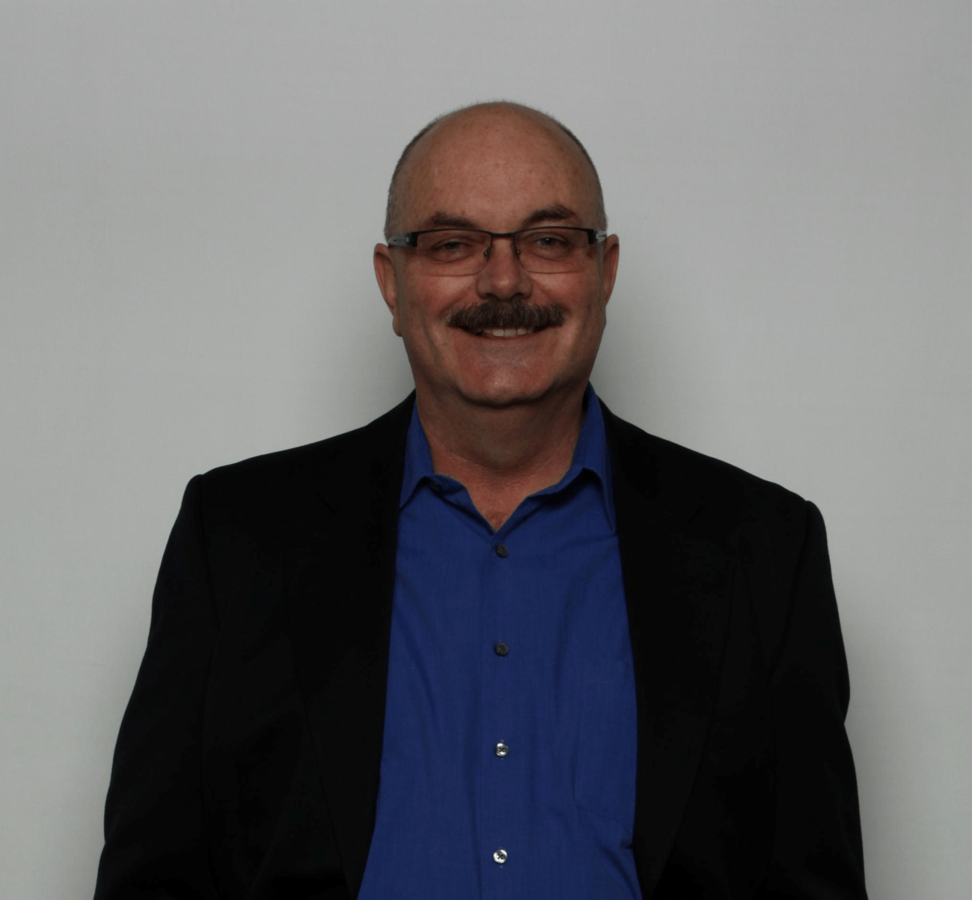 A man wearing glasses and a blue shirt is smiling for the camera