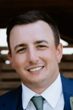 Man in blue suit, smiling. Outdoors, natural light.