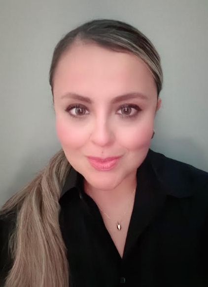 Blonde woman in green shirt smiles at the camera against a gray backdrop.