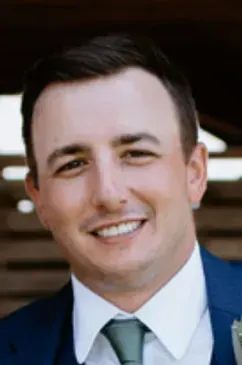 Man in blue suit, smiling. Outdoors, natural light.