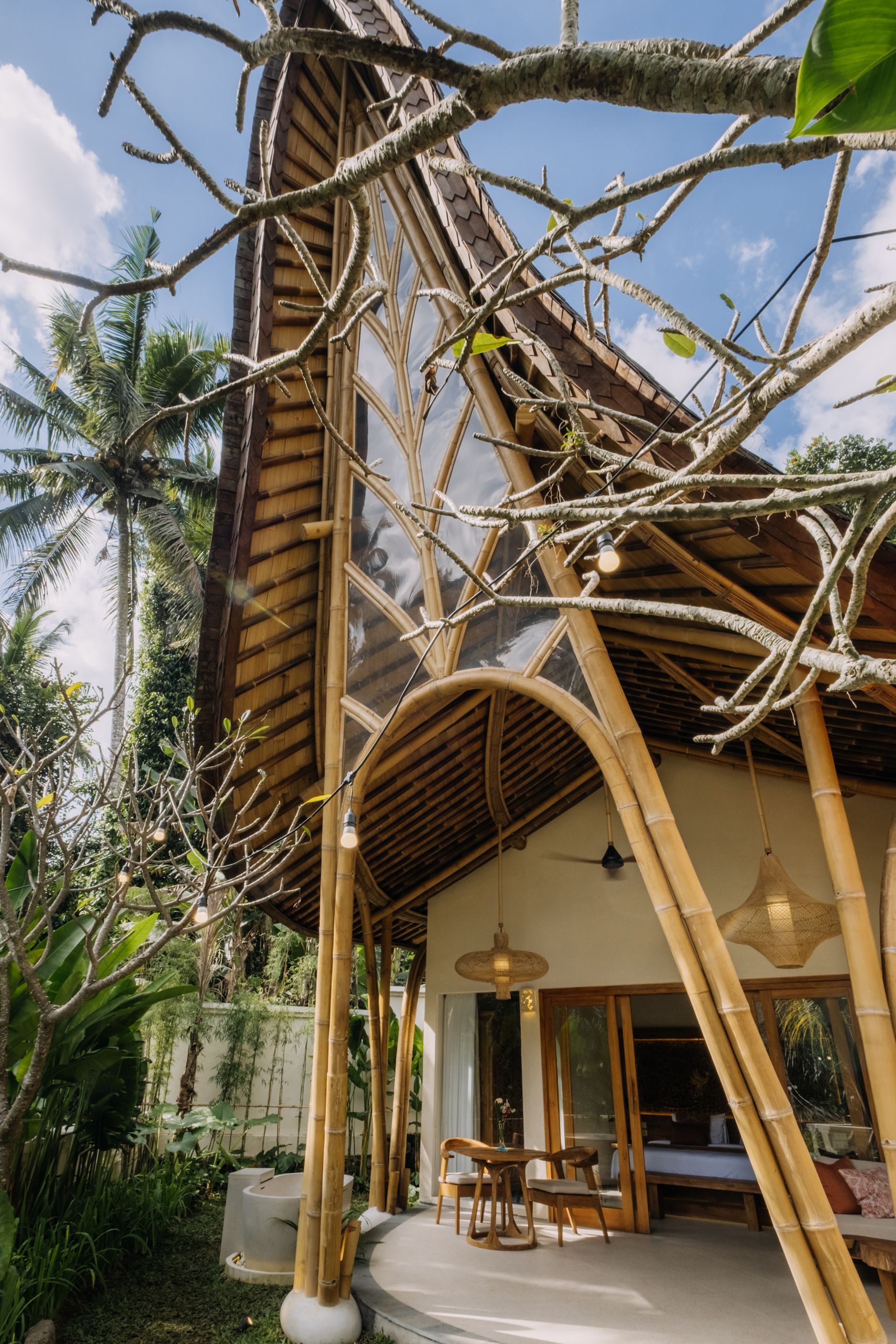 Tropical bamboo house with palm trees, open patio, and thatched roof under a clear sky