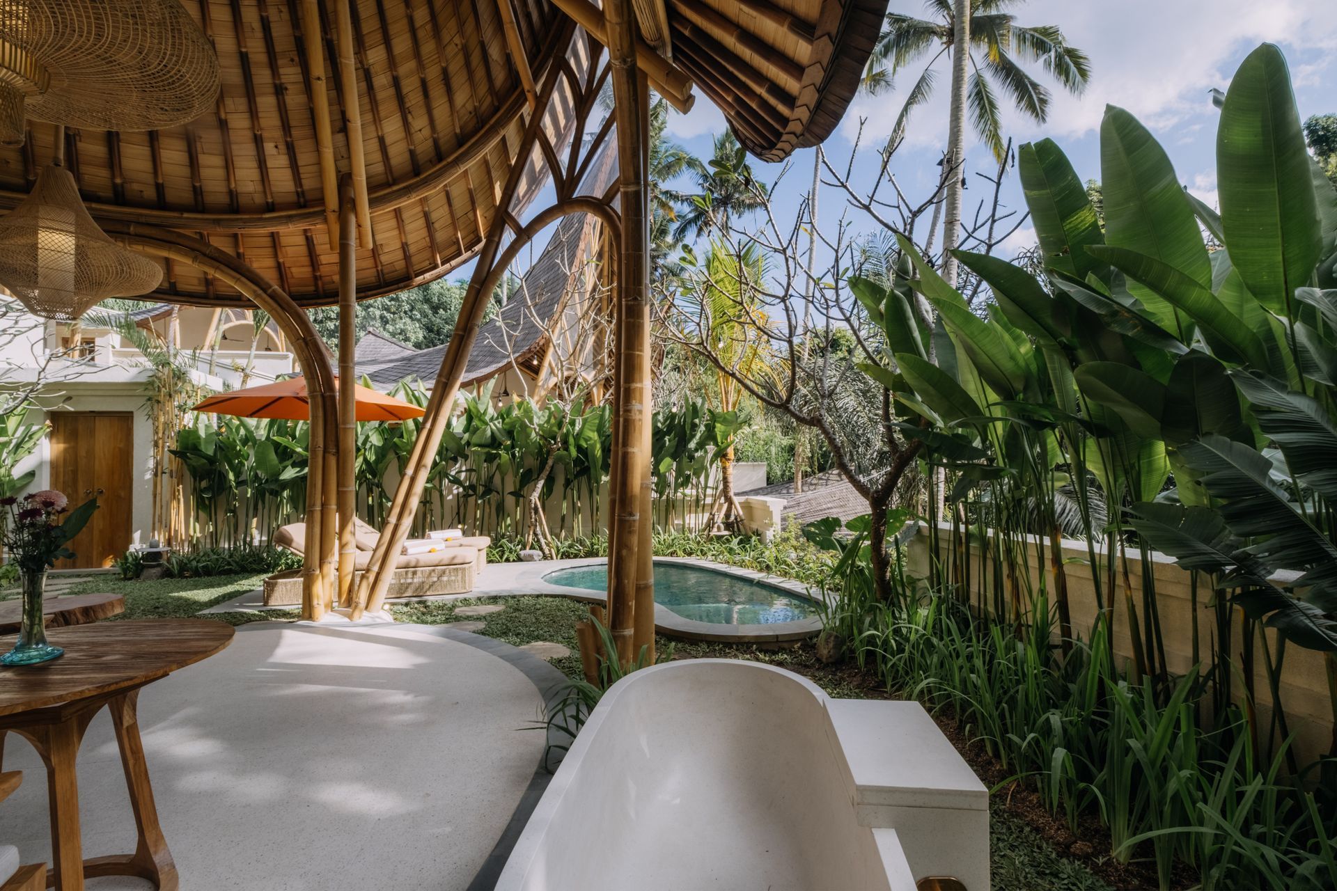 Tropical garden patio with bamboo roof, pool, and lush green plants