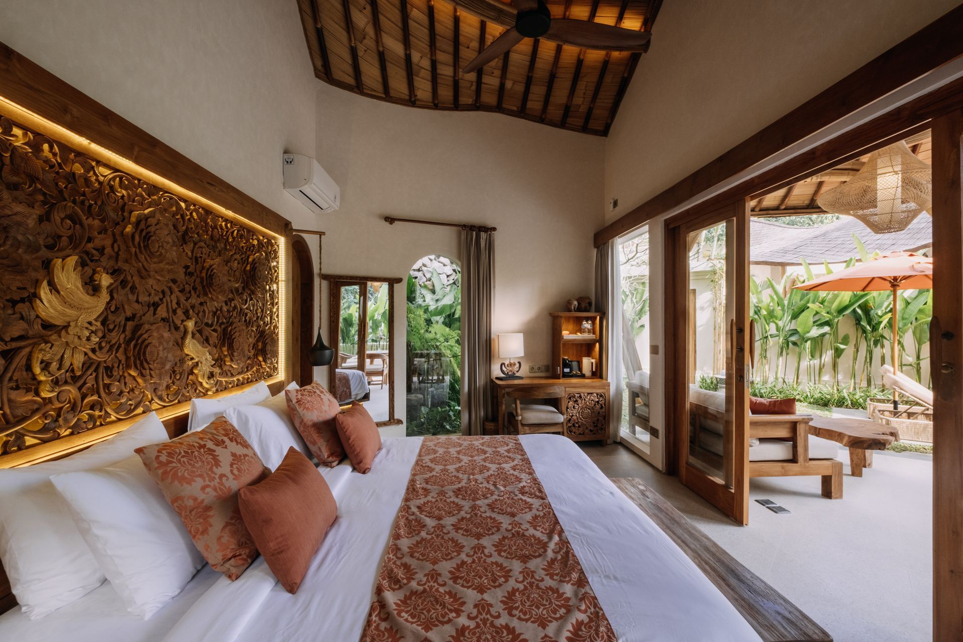 Luxury bedroom with carved wooden headboard, white bed, and open doors to a tropical patio