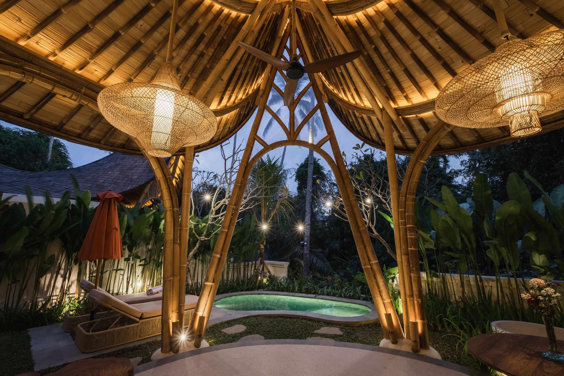 Tropical gazebo with woven bamboo roof, warm hanging lights, and a small pool at dusk
