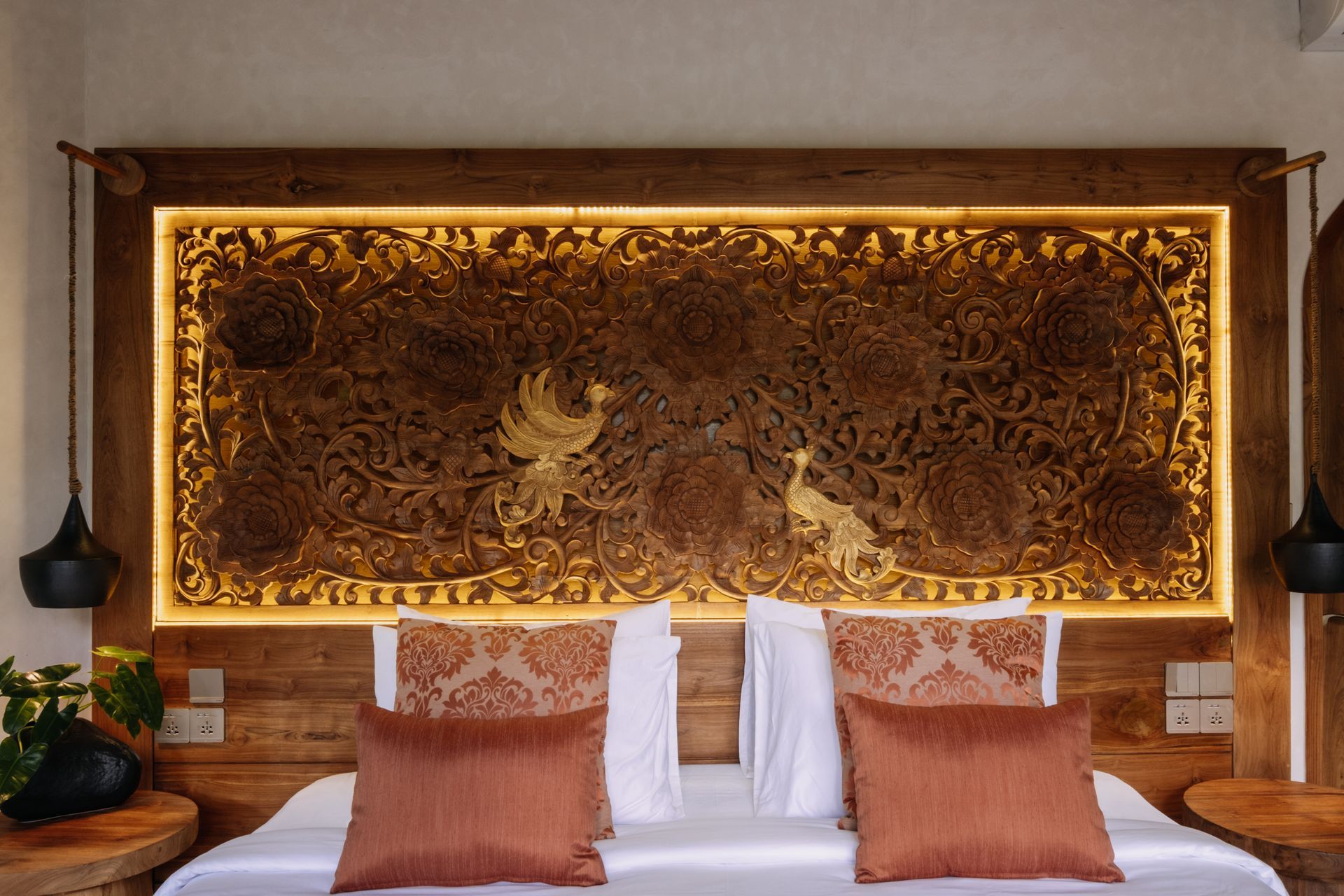 Hotel room headboard with ornate gold carved wall panel above two neatly made beds with rust pillows