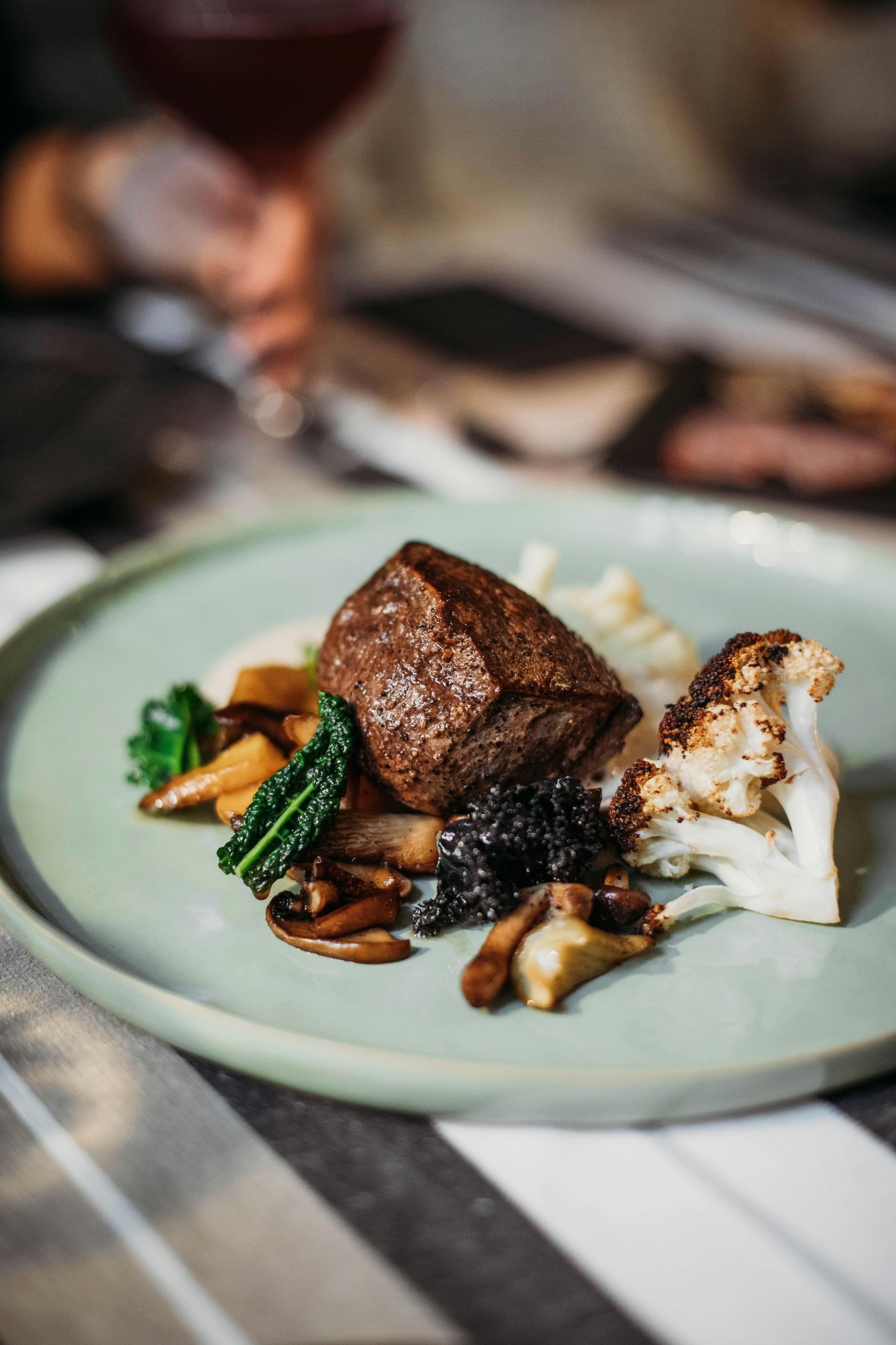 Plated gourmet meal with seared meat, white vegetables, and sauce on a pale green dish