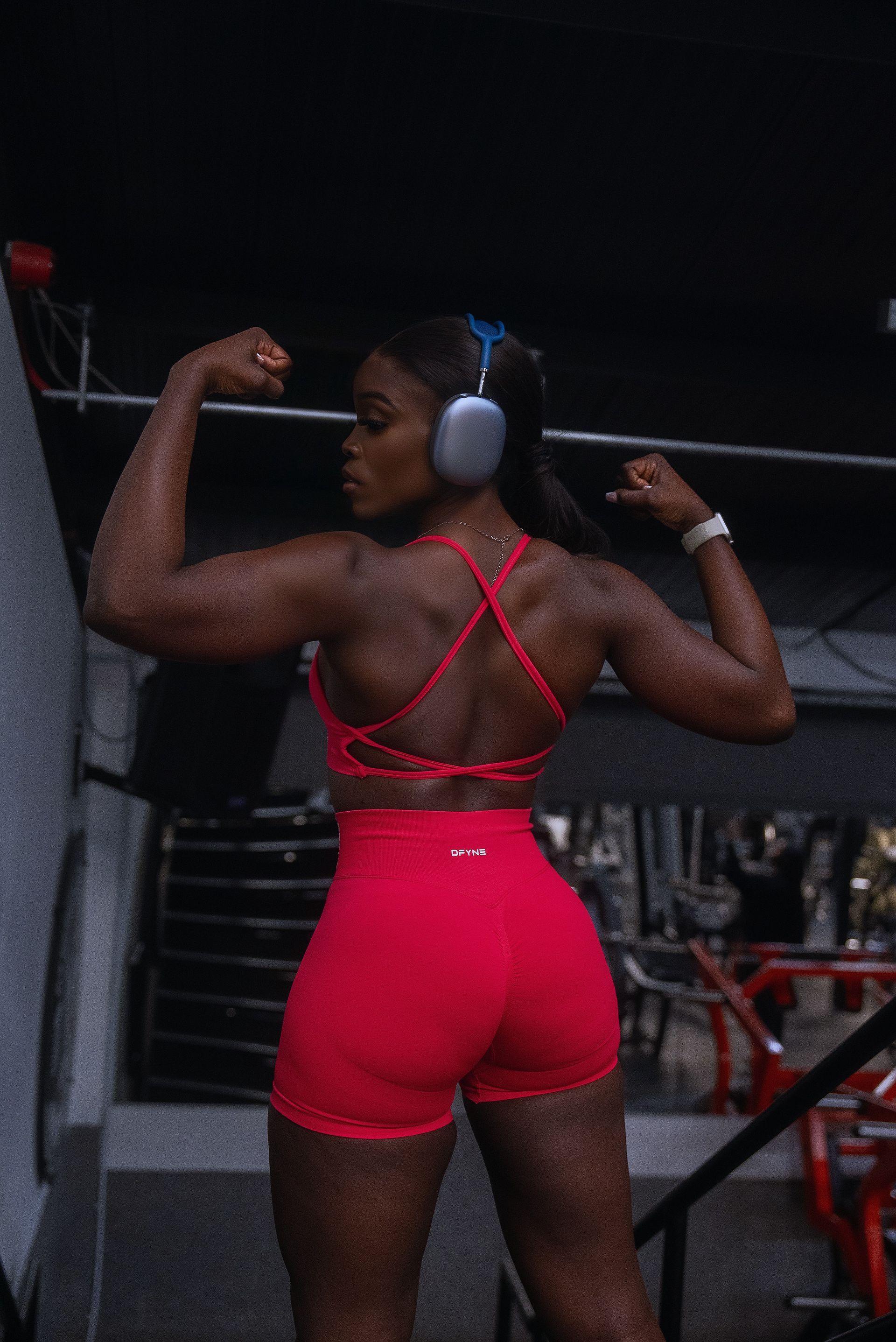 Nonye wearing headphones is flexing her muscles in a gym.