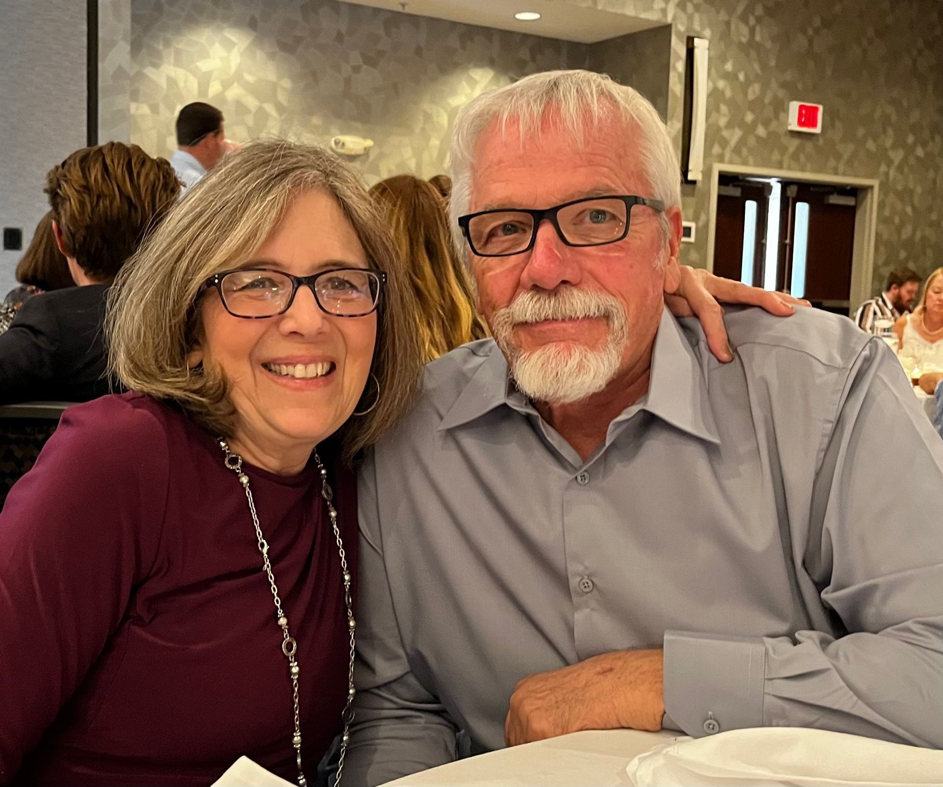 A man and a woman are posing for a picture while sitting at a table.