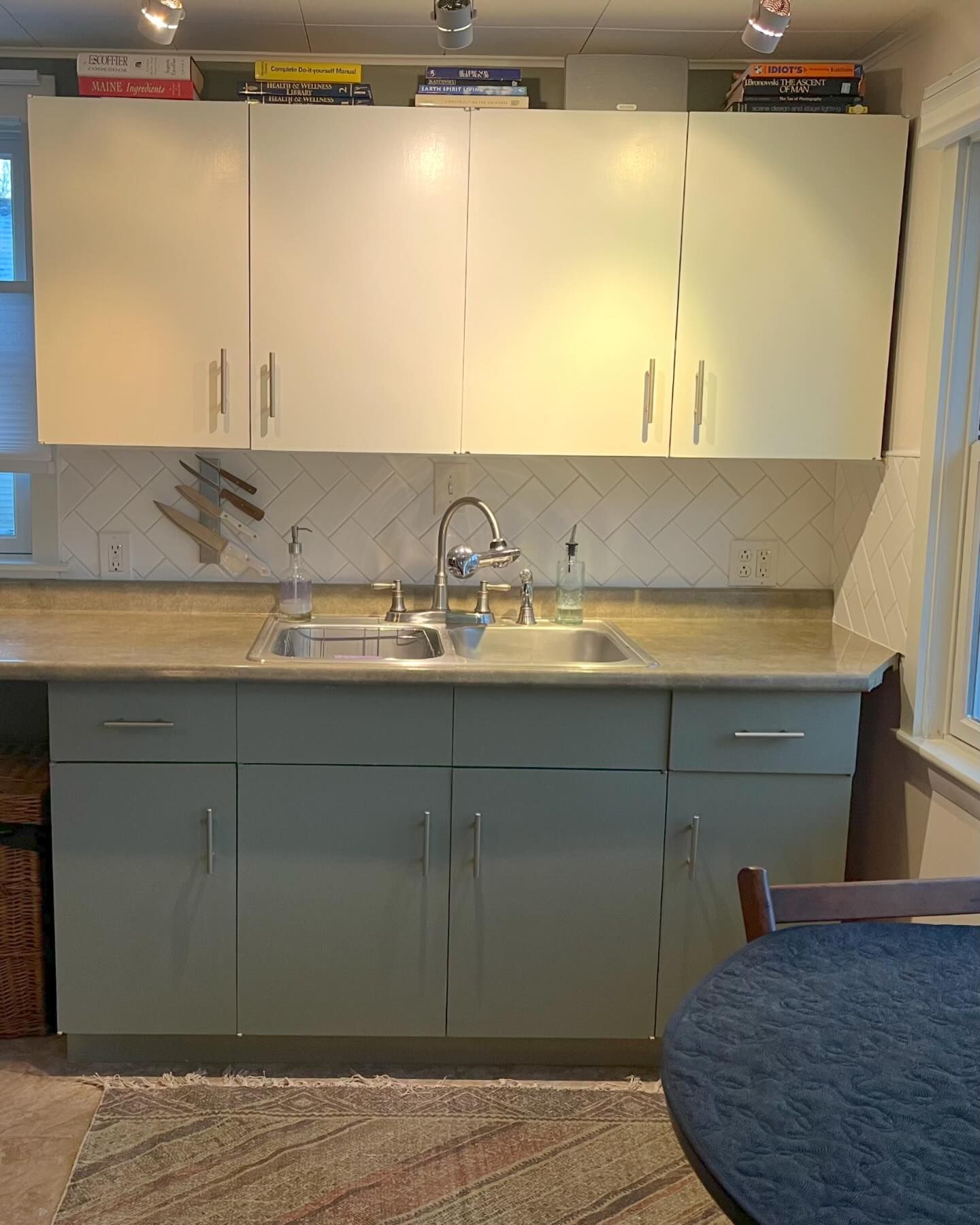 Kitchen with sage green lower cabinets, light upper cabinets, and a stainless steel sink.