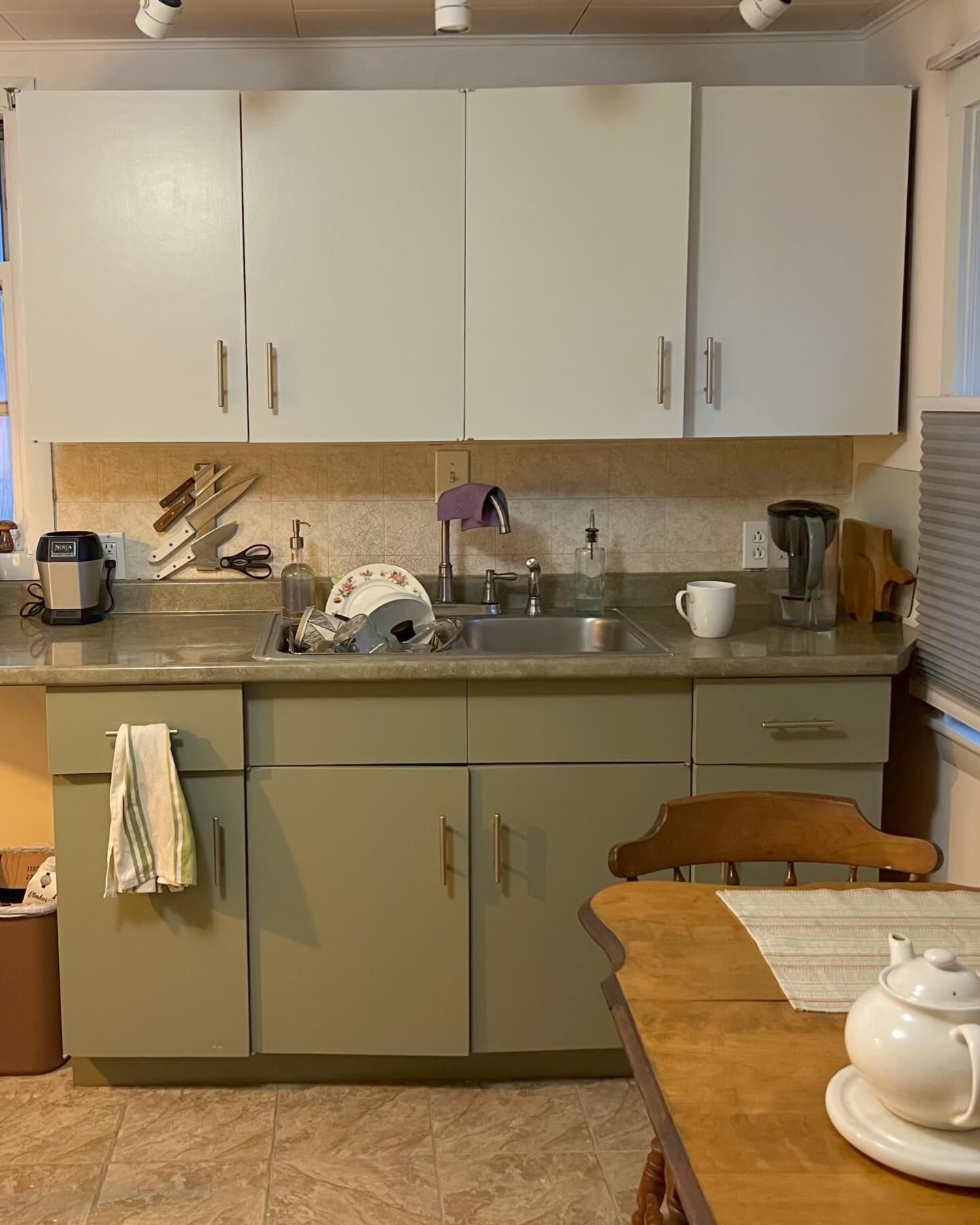 Kitchen with light green cabinets, white upper cabinets, sink, and a wooden table.