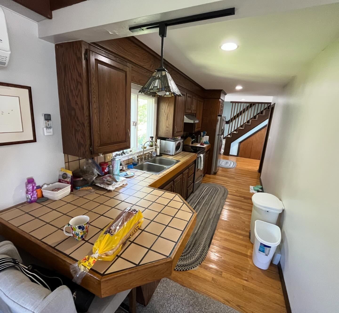 Kitchen with wooden cabinets, tile countertop, sink, and access to stairs.