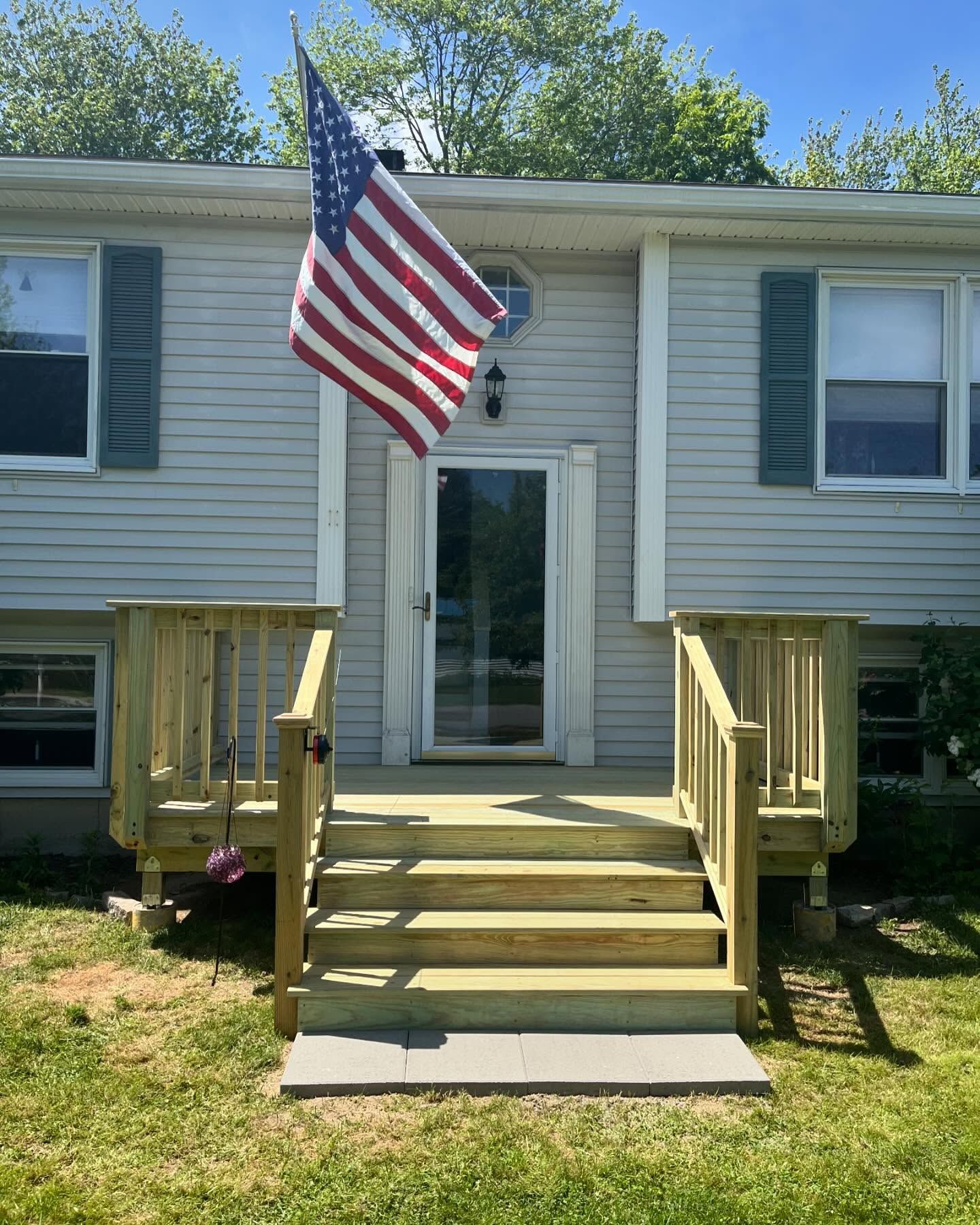 A two-story home with a new wooden porch, an American flag, and green shutters.