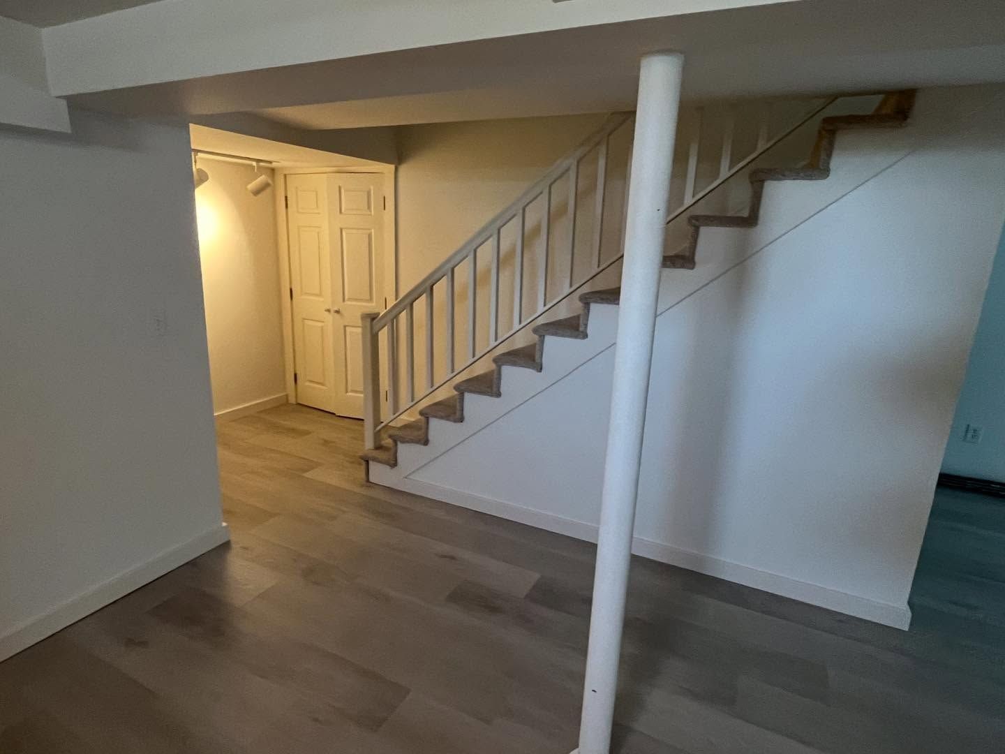 Interior view of a basement with stairs, a support column, and a doorway leading to a room with a closed door.
