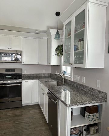 Kitchen with sage green cabinets, light countertops, and double sink. Books on upper white cabinets.