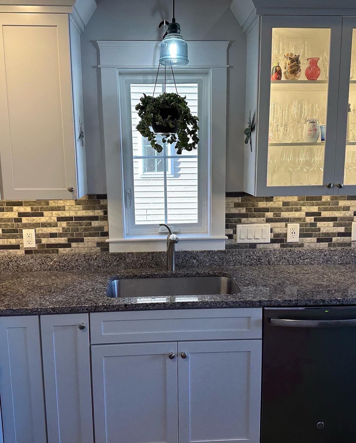 Kitchen with white cabinets, dark countertop, and sink under a window with a hanging plant.