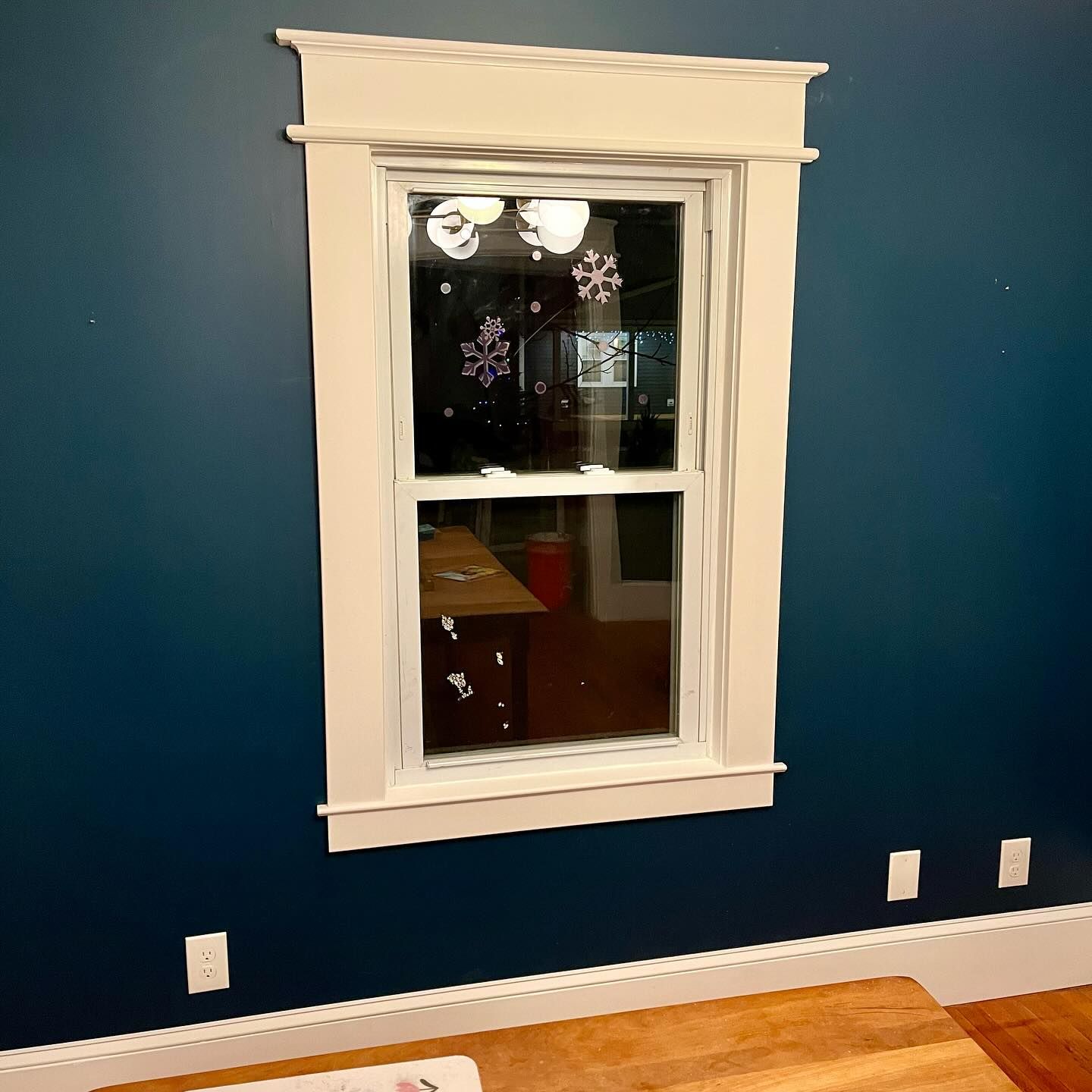 Window with white trim and snowflakes on a dark blue wall.