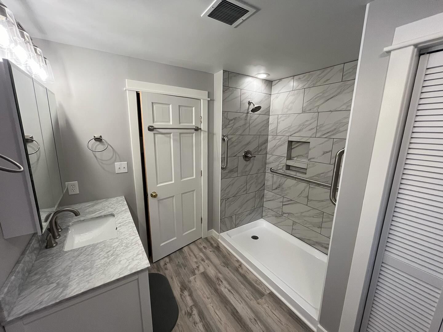 Bathroom with accessible shower, white vanity, and gray walls. Includes grab bars and a walk-in shower.