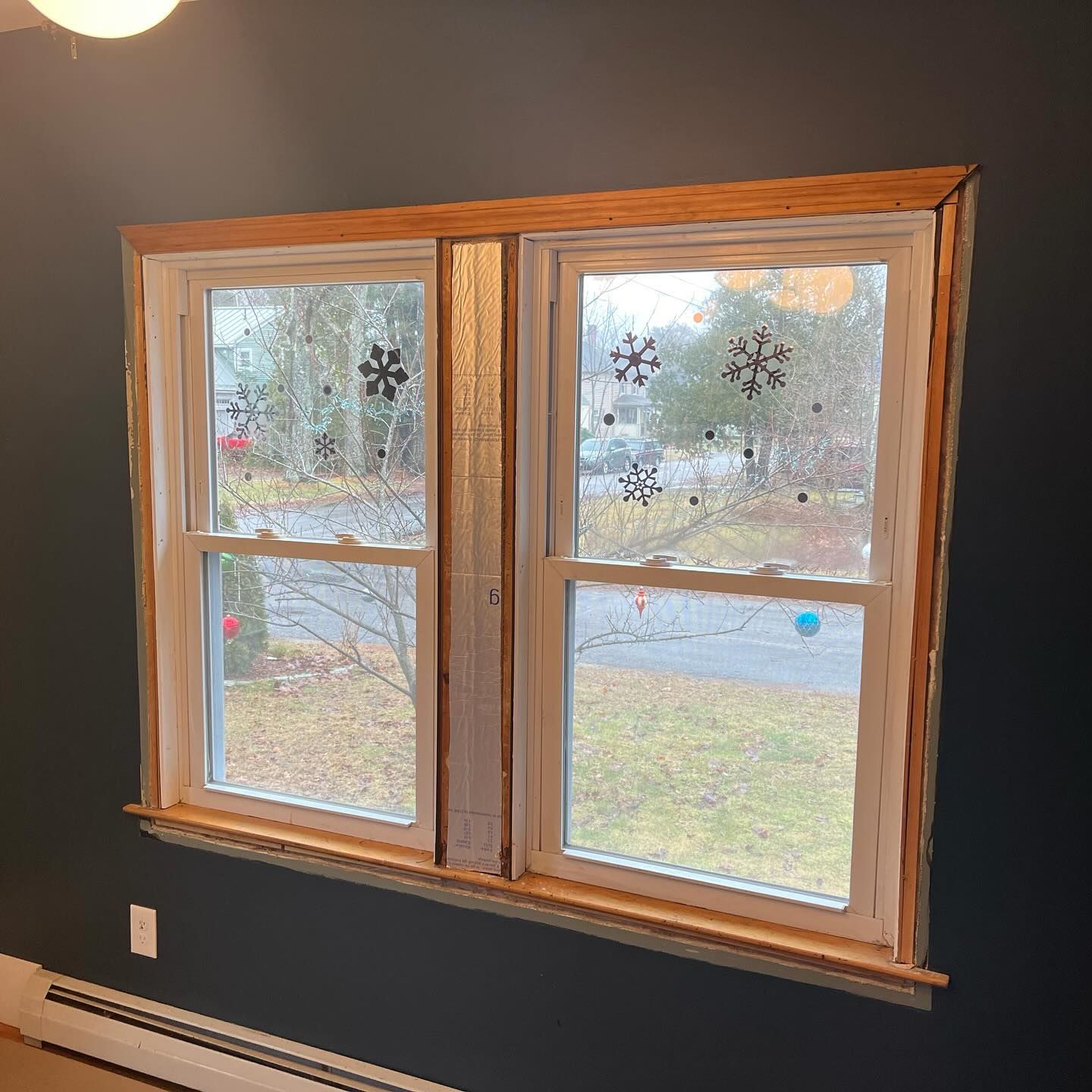 Two white-framed windows with wooden trim, decorated with snowflake cutouts, against a dark blue wall.