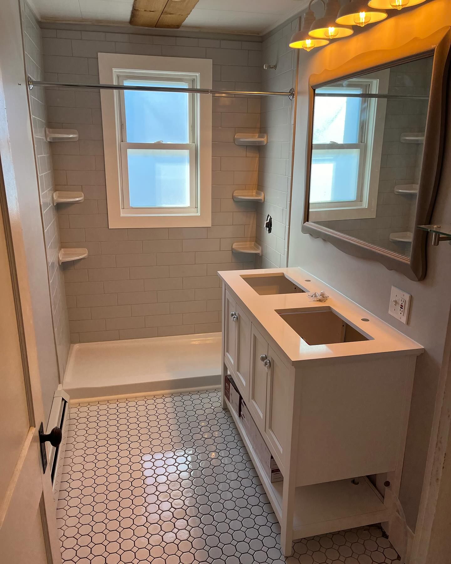Bathroom with white double vanity, shower with shelves, and black and white floor tiles.