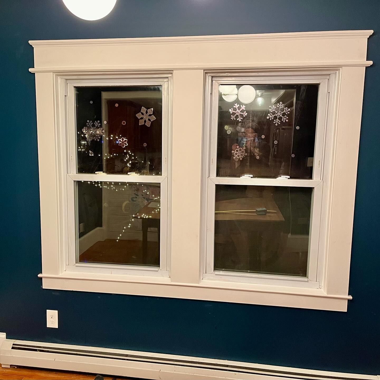 Two white-framed windows with snowflake decorations against a dark blue wall.