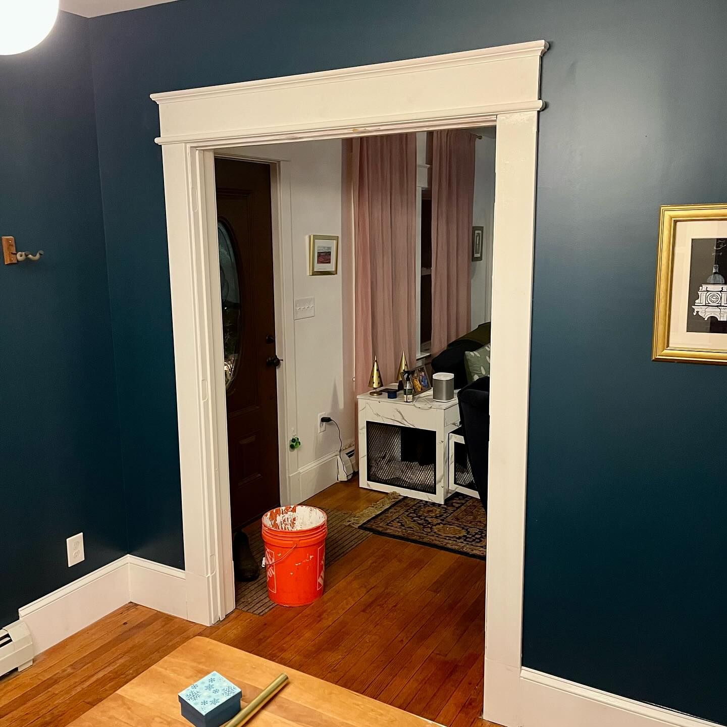 Dark blue room doorway with white trim; view into a room with pink curtains and a cabinet.