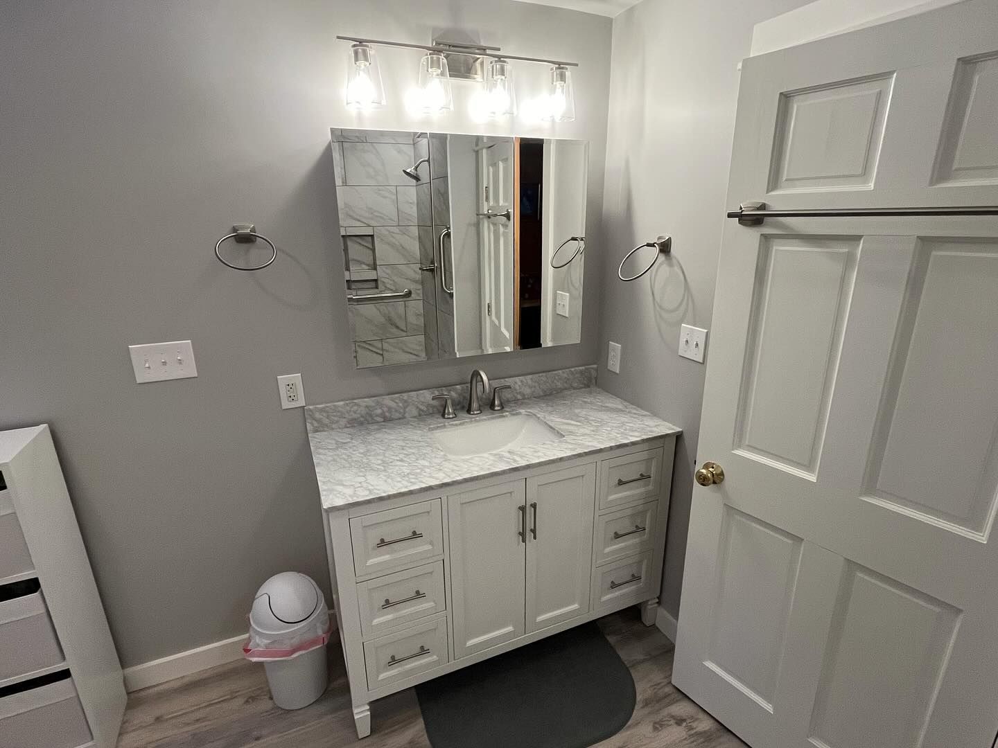 Bathroom with gray vanity, mirror, lights, and closed door.