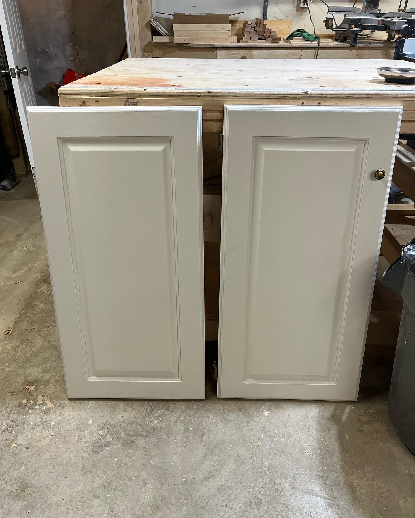 Two off-white cabinet doors resting against a wooden surface, with a brass knob on one.