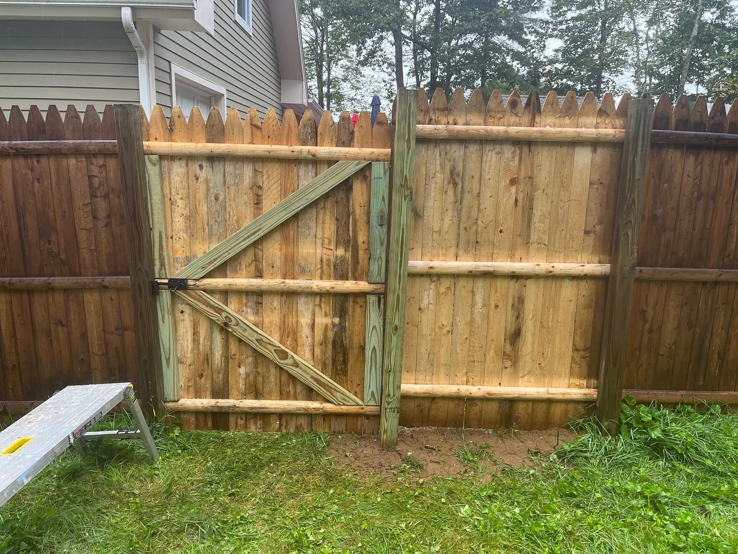 Wooden fence with gate, set in grass. The gate is open, and a small white stool sits nearby.