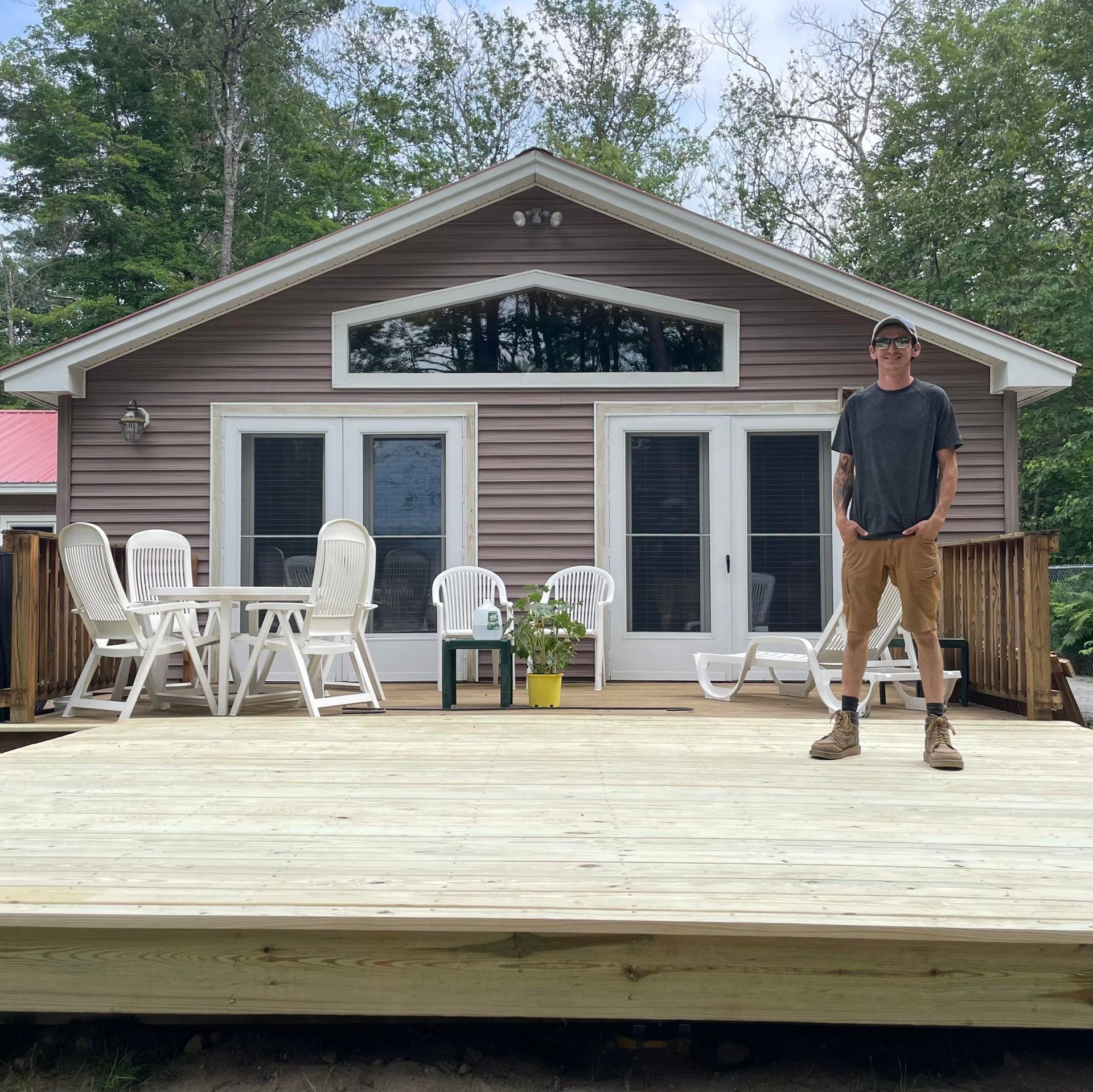 Man on deck in front of a small house with double doors, white chairs, and a triangular window.