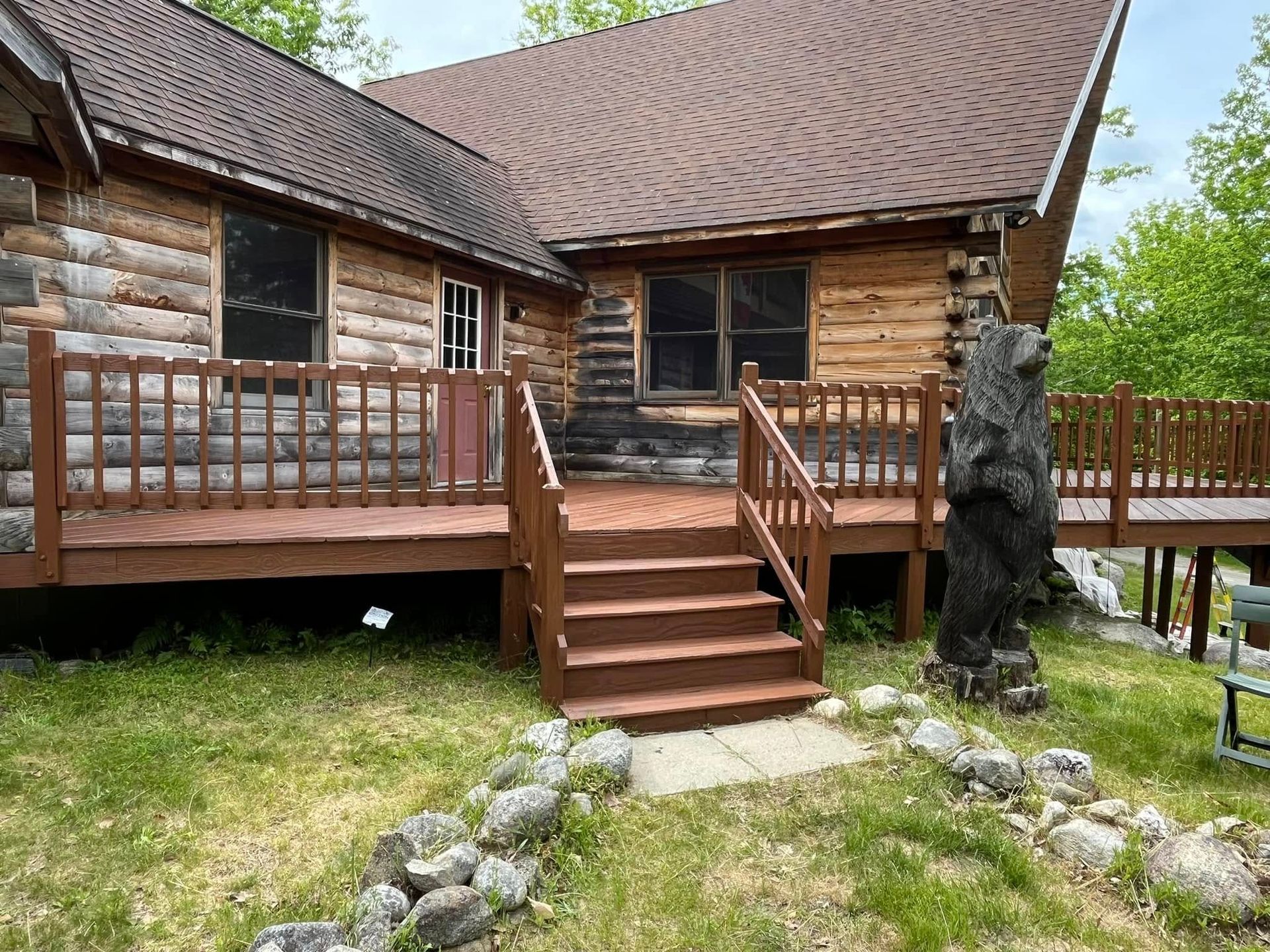 Log cabin with a brown deck and steps leading to the entrance, a carved bear statue stands to the side.